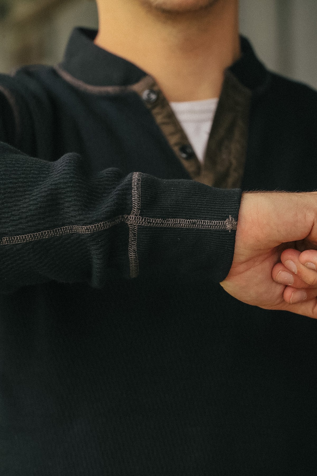 Close-up of a person wearing a dark charcoal ribbed knit quarter-zip pullover sweater with contrast stitching and a patterned collar, layered over a white undershirt.