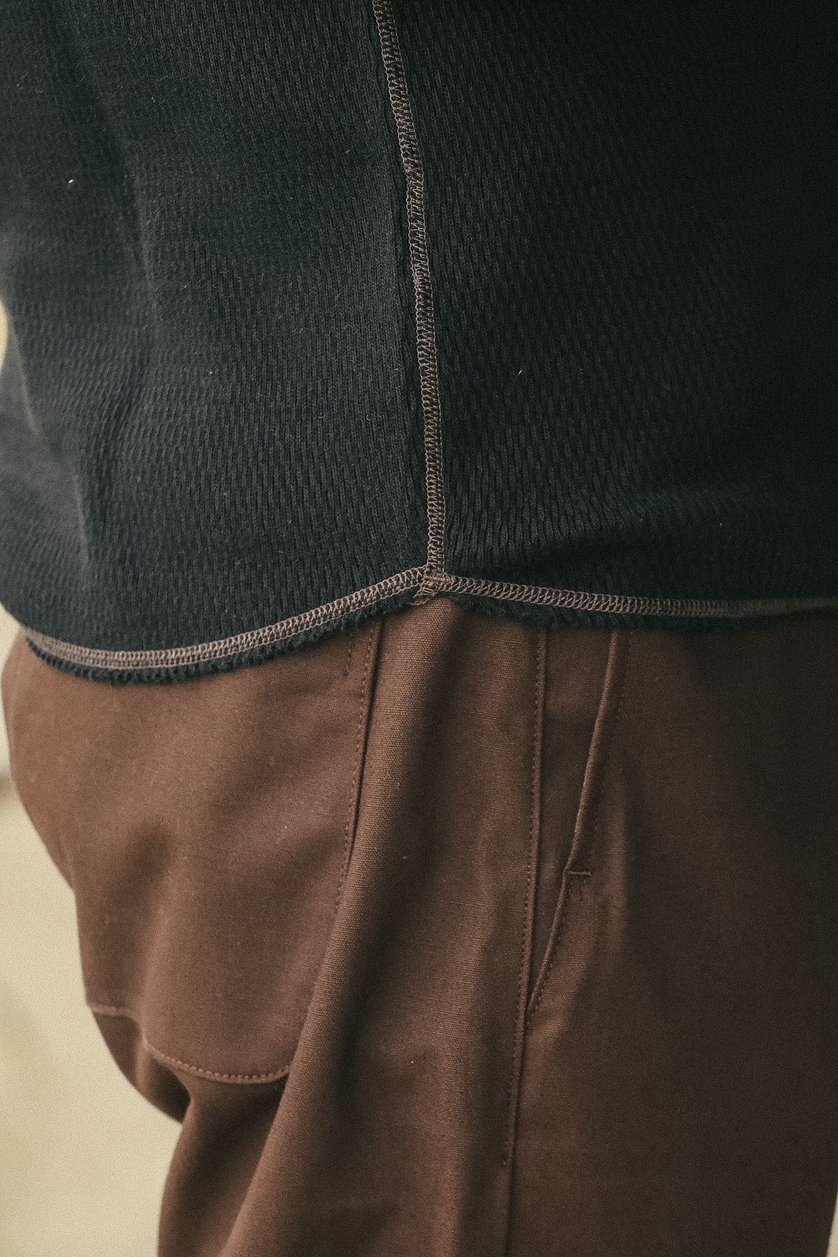 Close-up detail of a person wearing a dark charcoal knit top with brown pants, showing the textured fabric and seams.