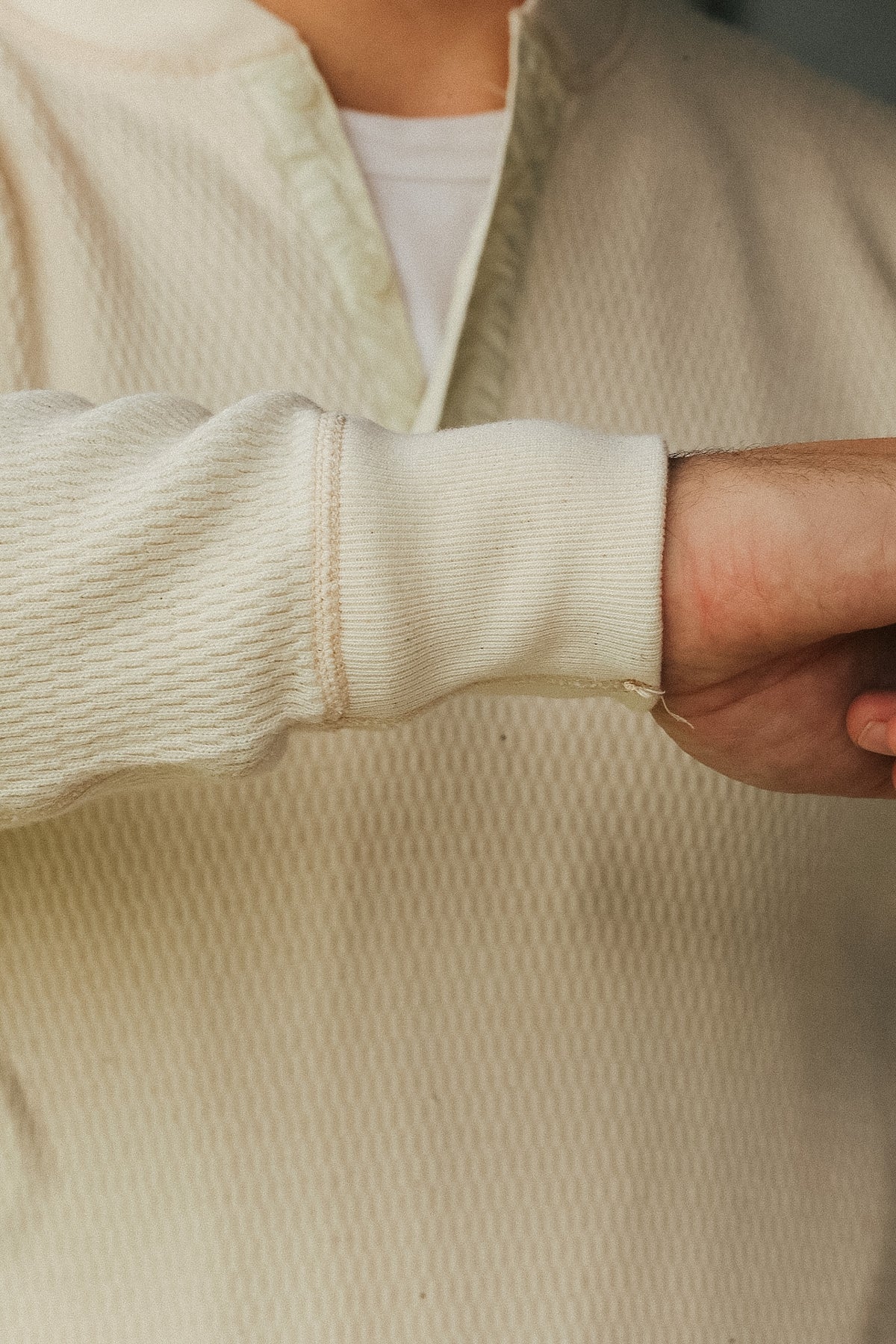 Close-up of a person wearing a cream-colored textured quarter-zip pullover sweater with a ribbed cuff, layered over a white t-shirt.