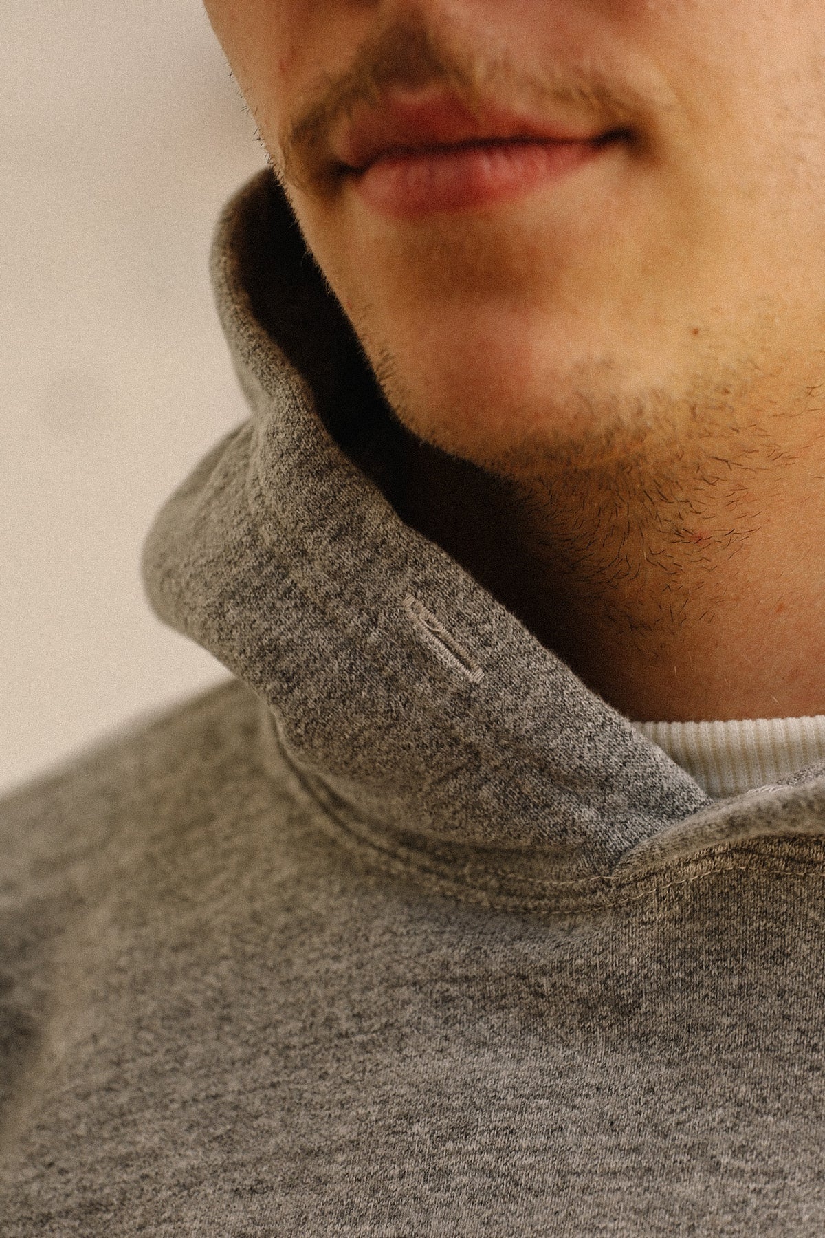 Close-up of a person wearing a heather gray pullover hoodie with a ribbed white undershirt, showing the collar and lower face.