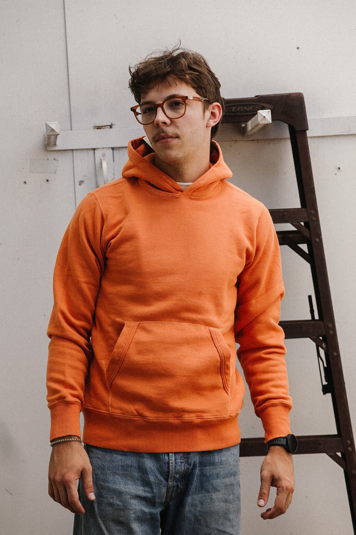 man wearing an orange sweater and jeans on a white backdrop
