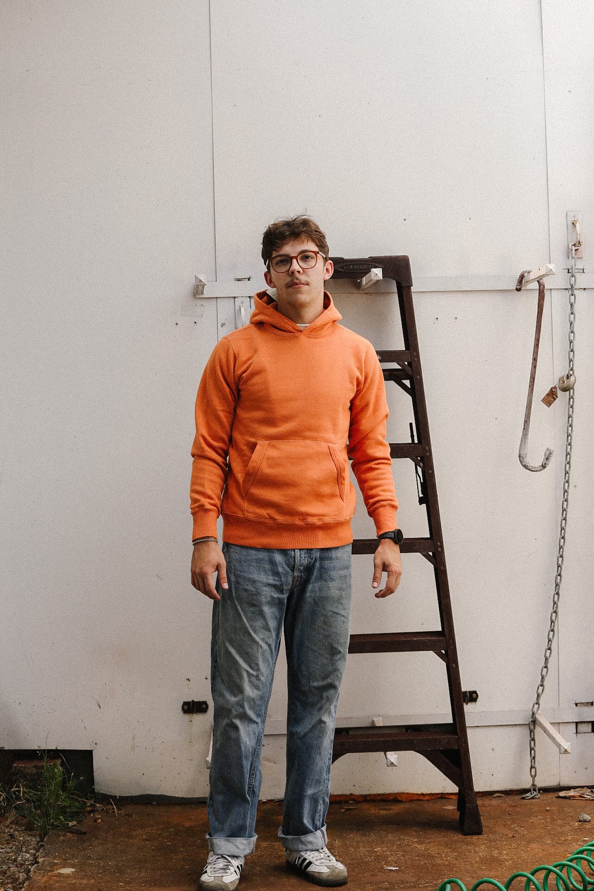man wearing an orange sweater and jeans on a white backdrop