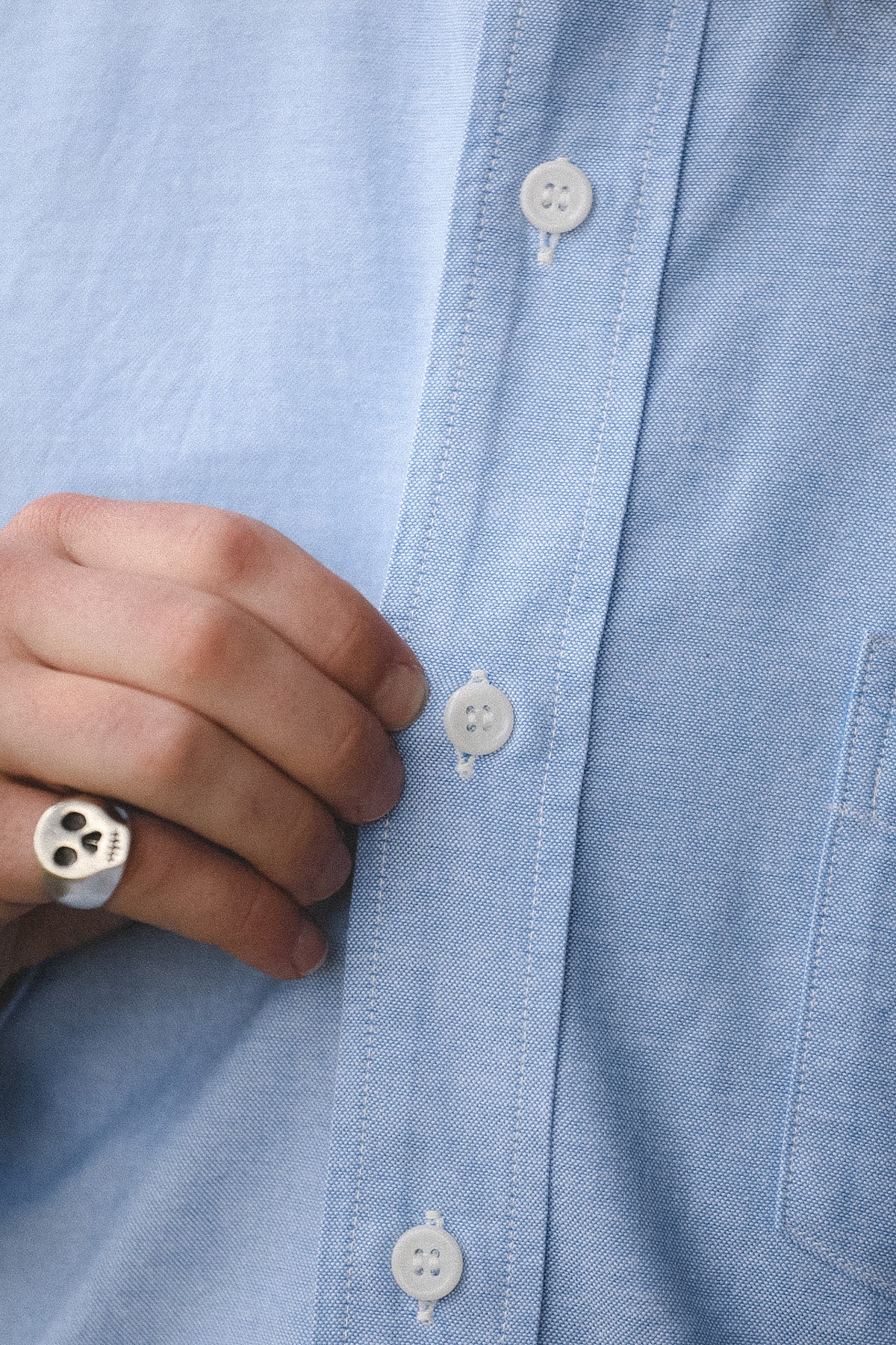 Close-up of a person buttoning a light blue shirt with a blurred background