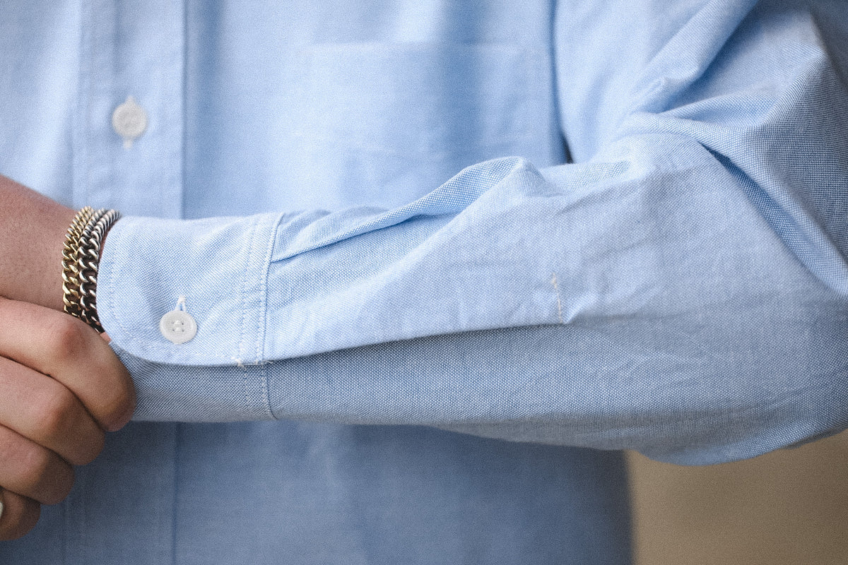 Light blue shirt with rolled-up sleeve and hand wearing a gold bracelet.