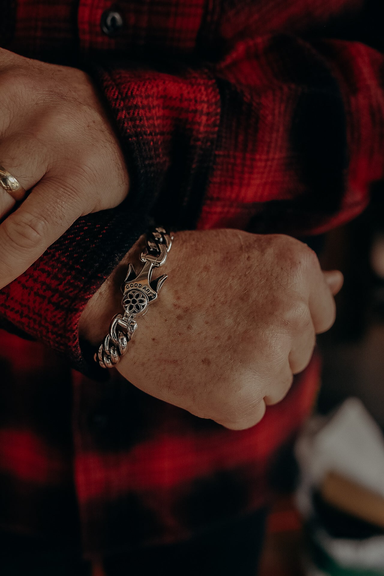 Close-up of hand wearing a silver chain bracelet with a decorative clasp and red plaid shirt sleeve