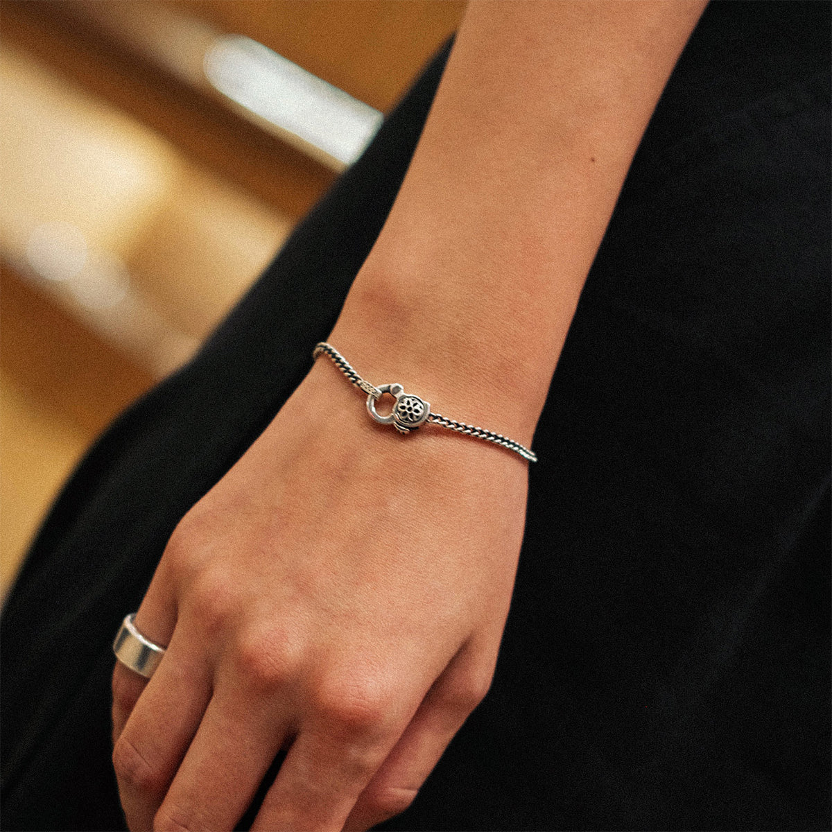 Close-up of a wrist wearing a silver curb chain bracelet with a decorative clasp and a silver ring on the hand