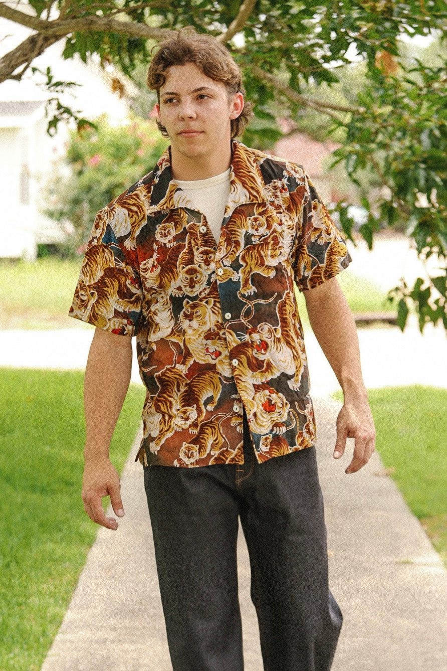Young man wearing a short-sleeve painted tiger pattern shirt outdoors on a sidewalk with greenery