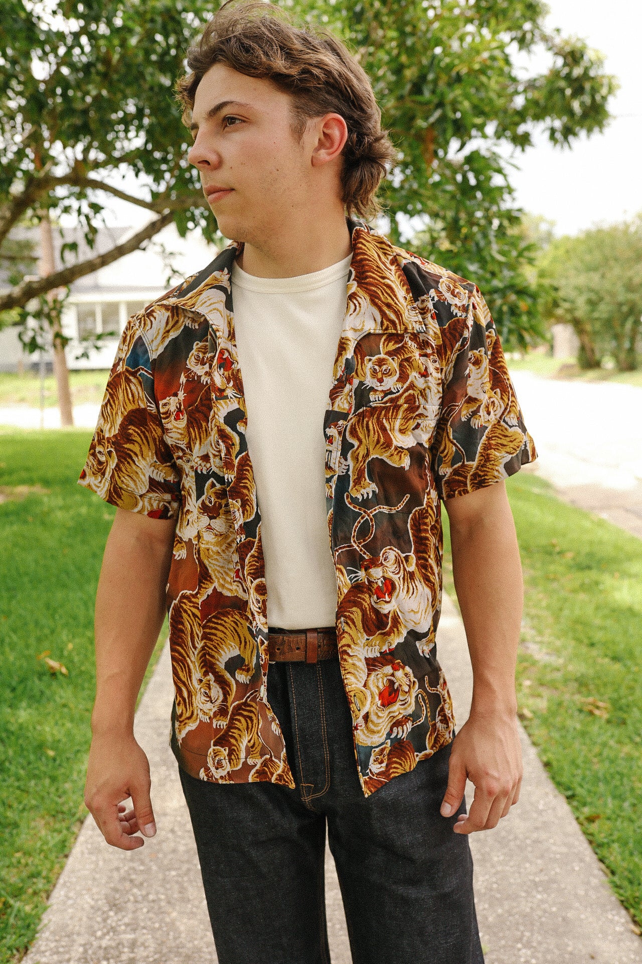 Young man wearing a tiger print short-sleeve shirt over a white tee, standing outdoors on a sidewalk