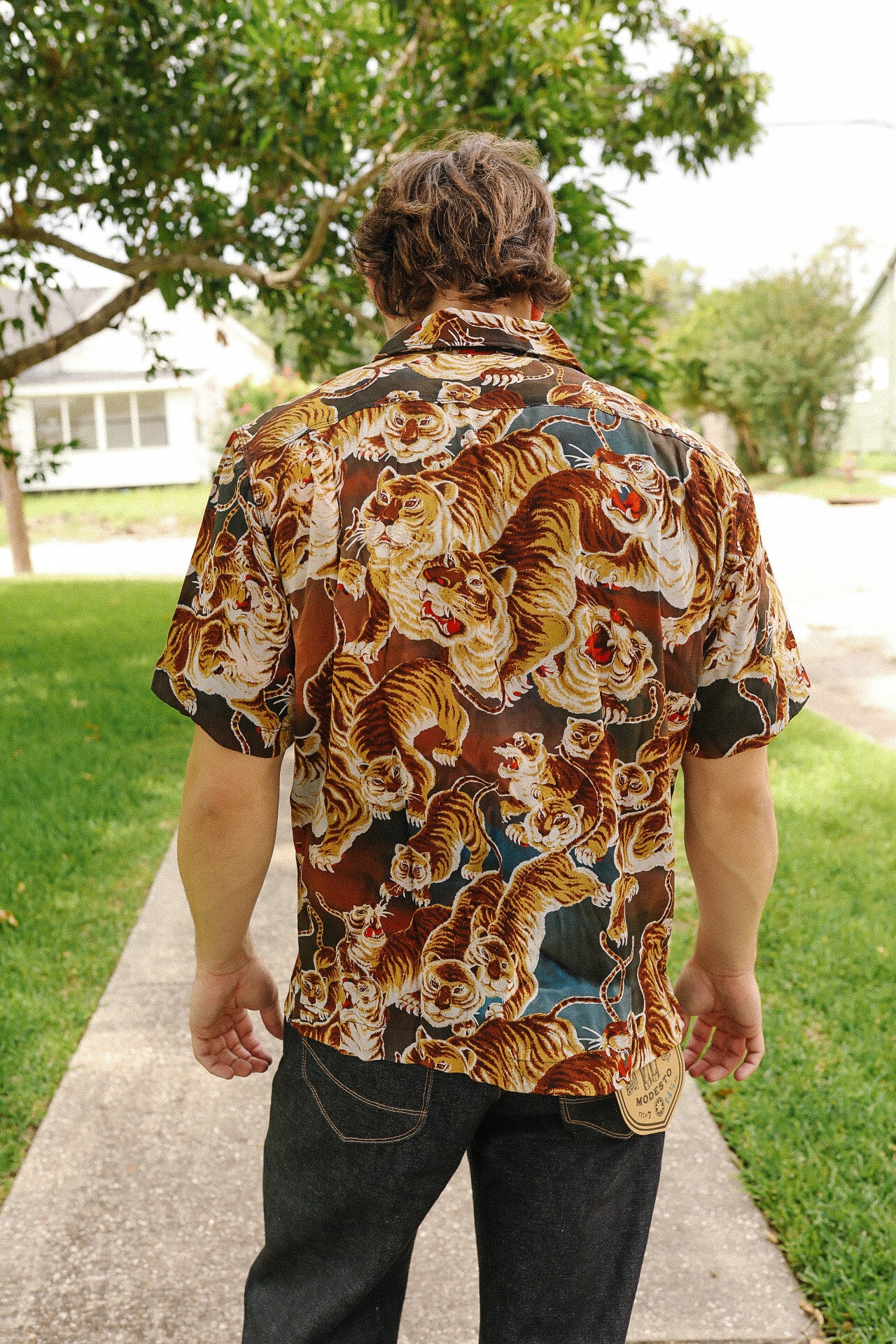 Man wearing a short-sleeve button-up shirt with a bold painted tiger print walking outdoors on a sidewalk