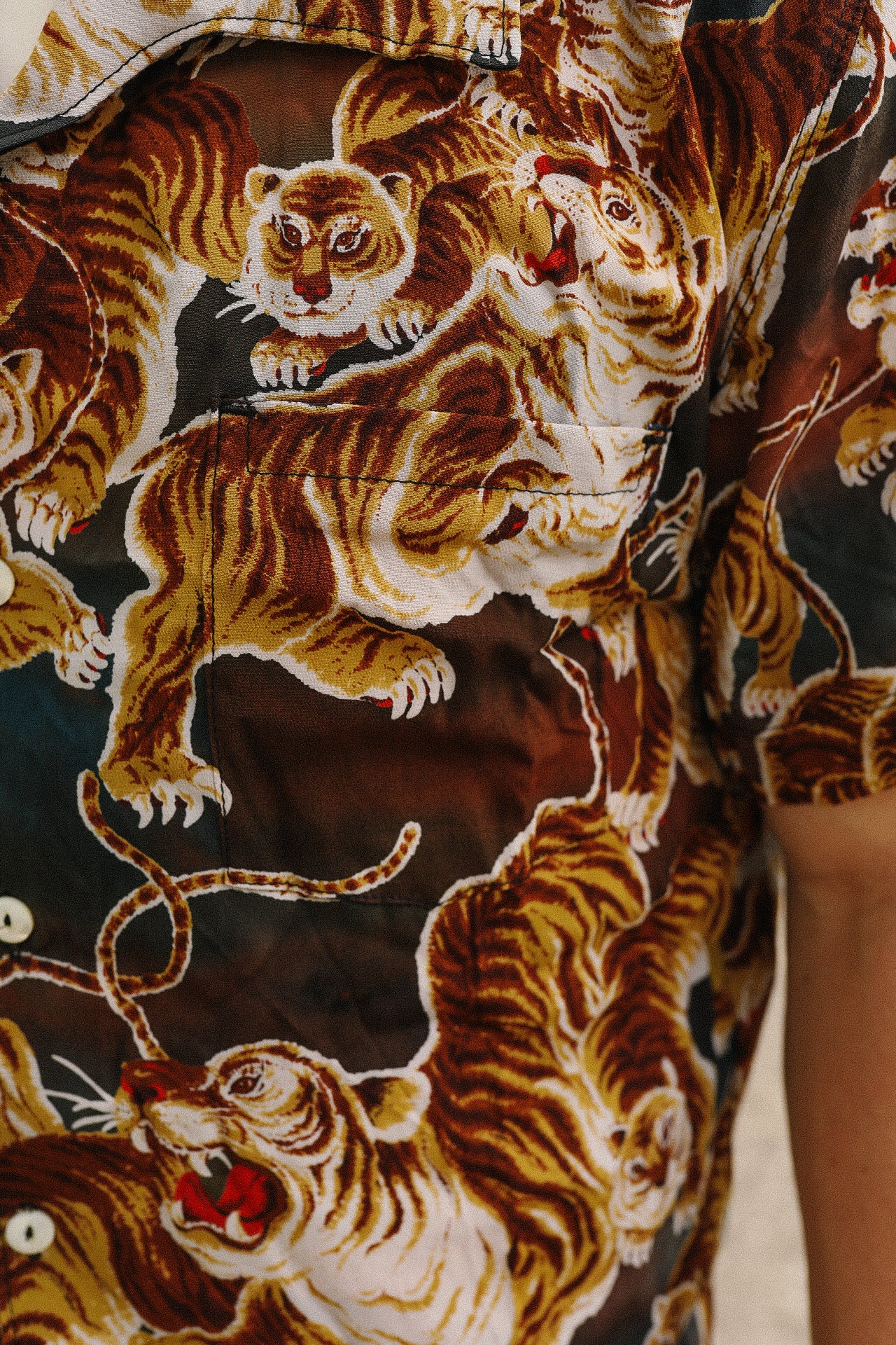 Close-up of shirt fabric with vivid orange and brown painted tiger pattern and front pocket detail