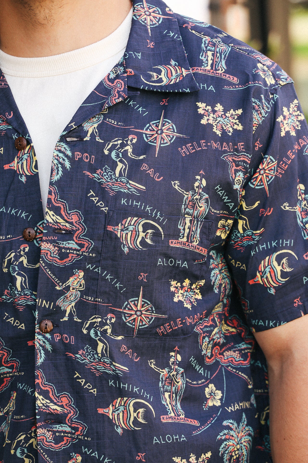 Close-up of navy Hawaiian shirt with colorful island map print, surf and compass motifs