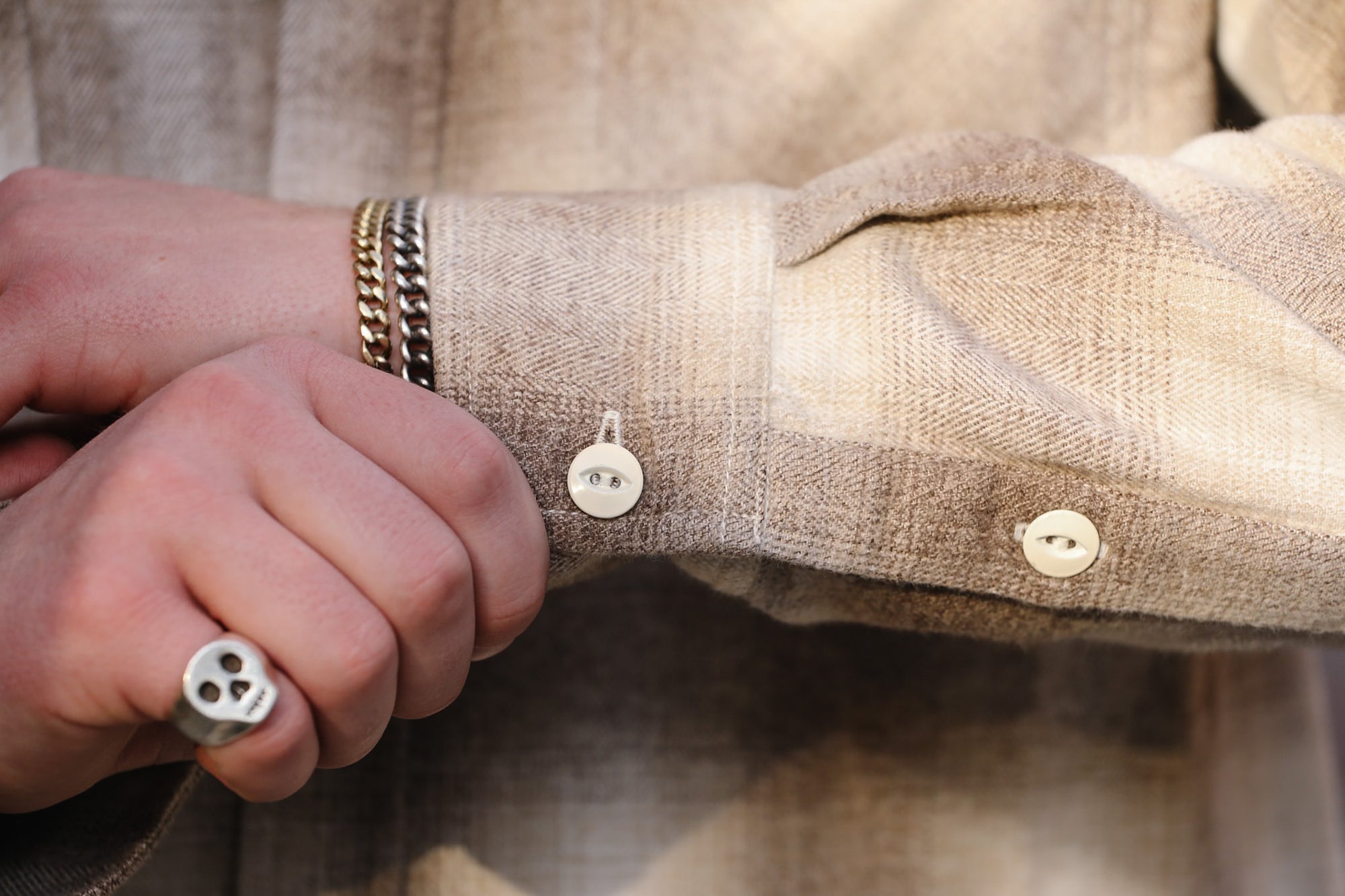 Close-up of a person wearing a beige shirt with buttons and a bracelet.