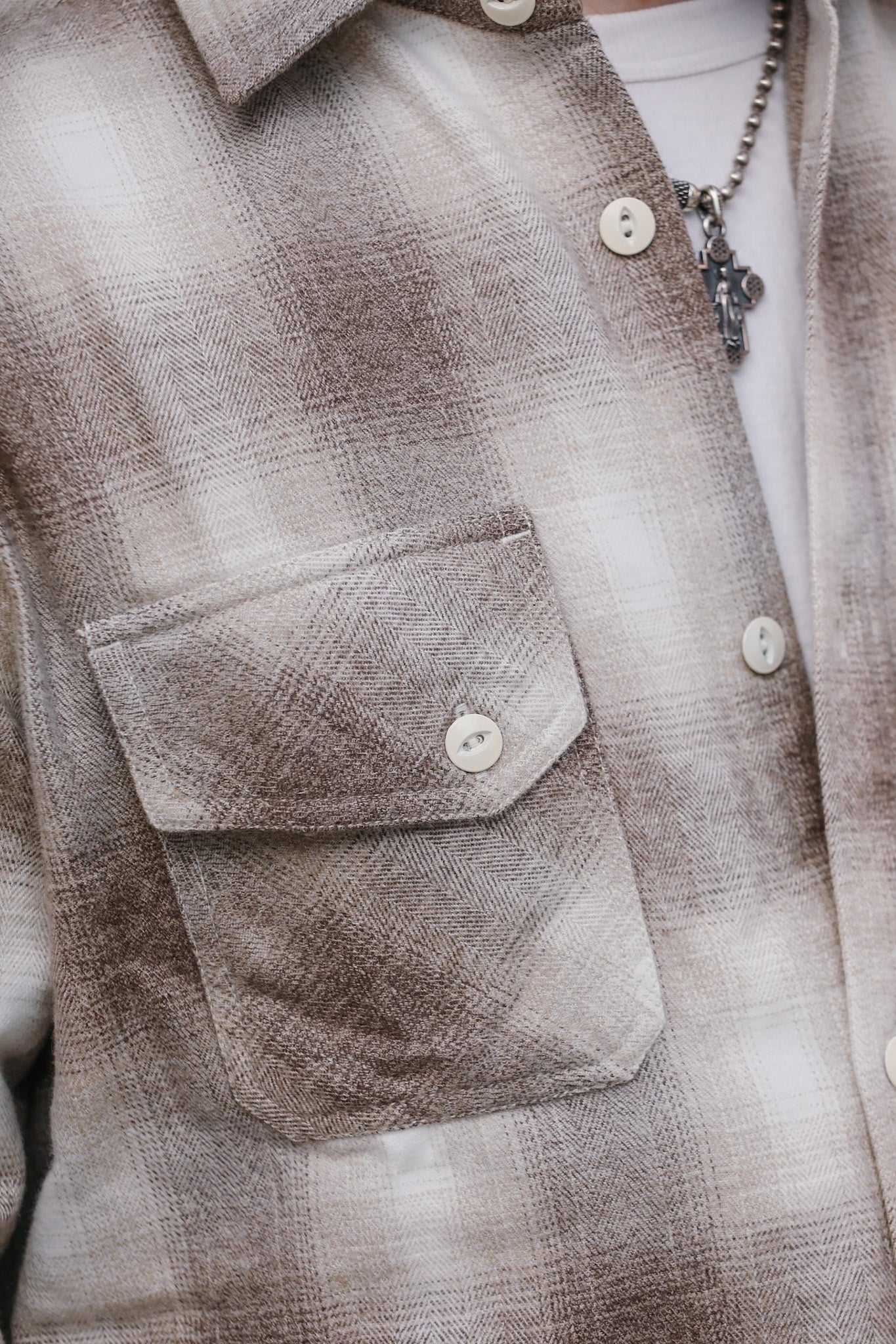 Close-up of a brown plaid shirt with a pocket and buttons.