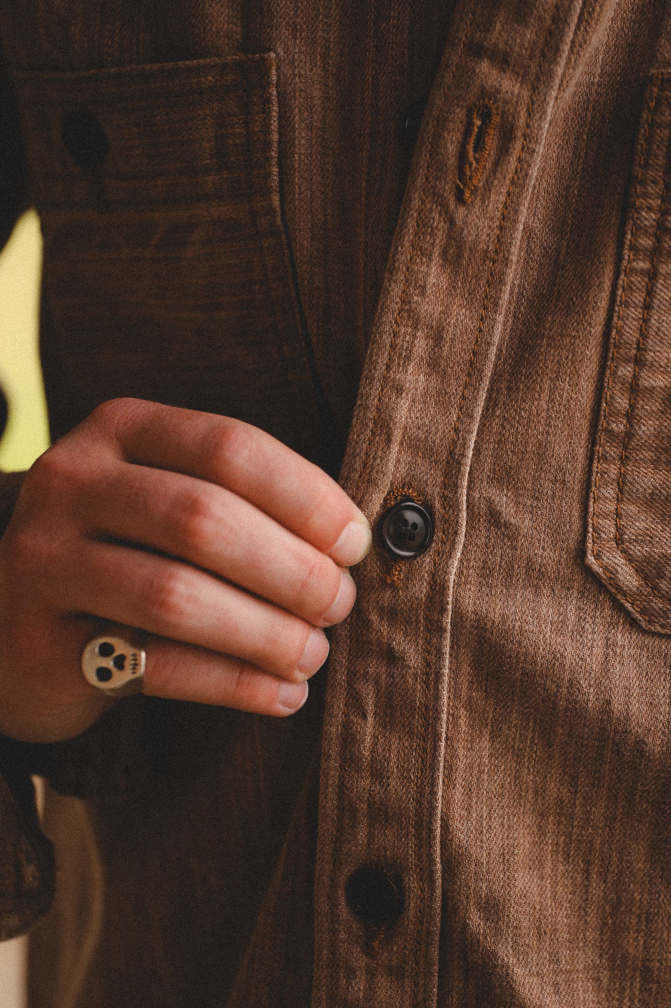 Close-up of a hand buttoning a brown jacket
