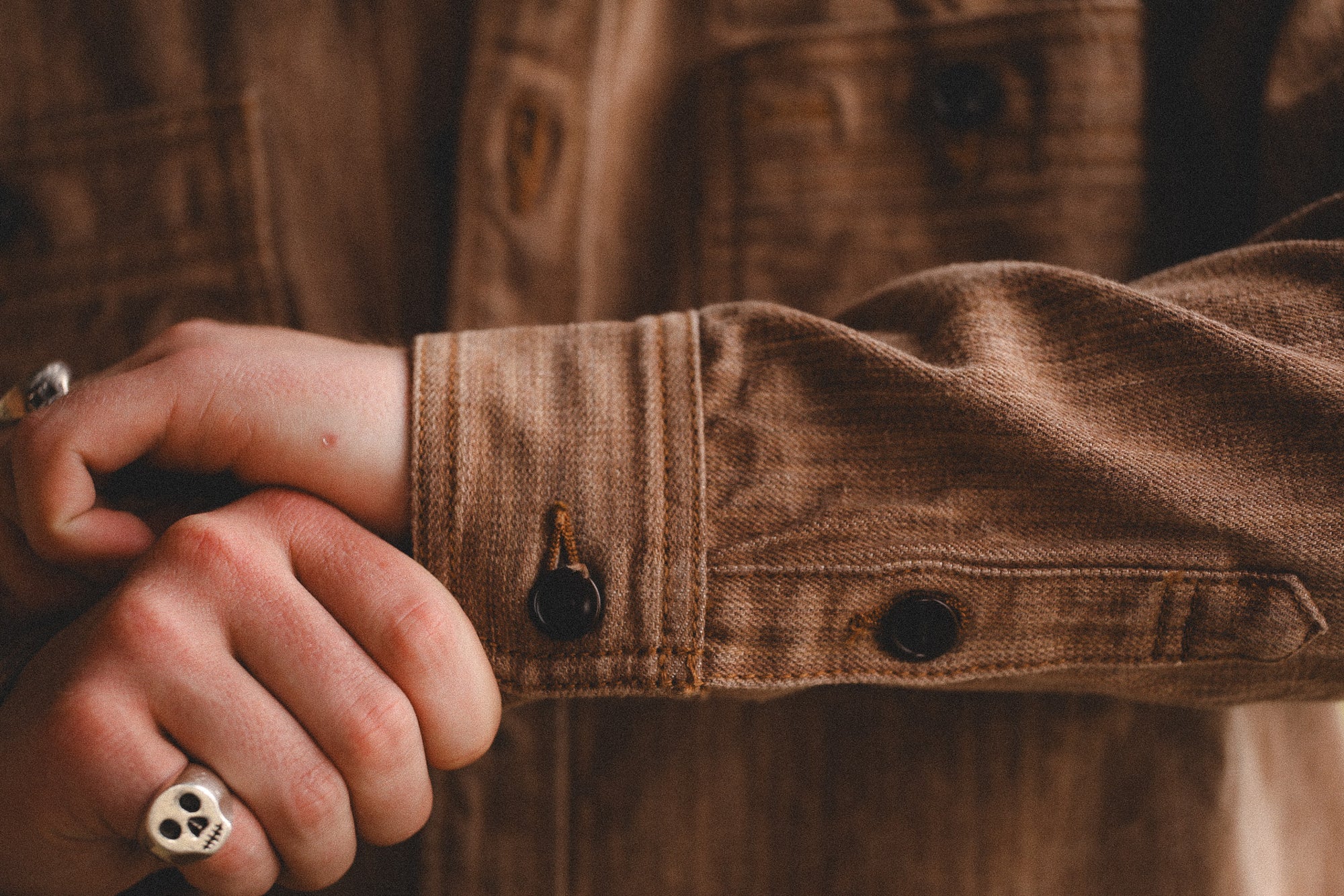 Close-up of a person wearing a brown jacket with rolled-up sleeves, focusing on the arm and hand.
