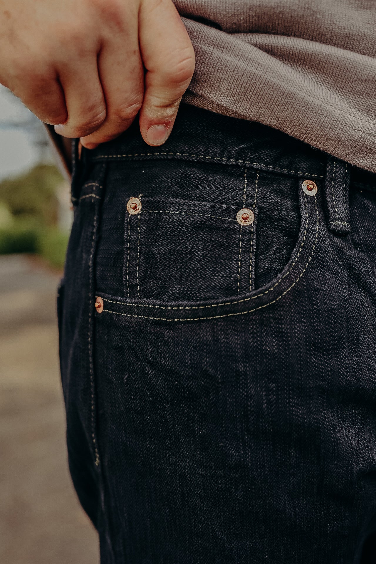 Close-up of hand adjusting dark raw denim jeans with classic stitching and copper rivets