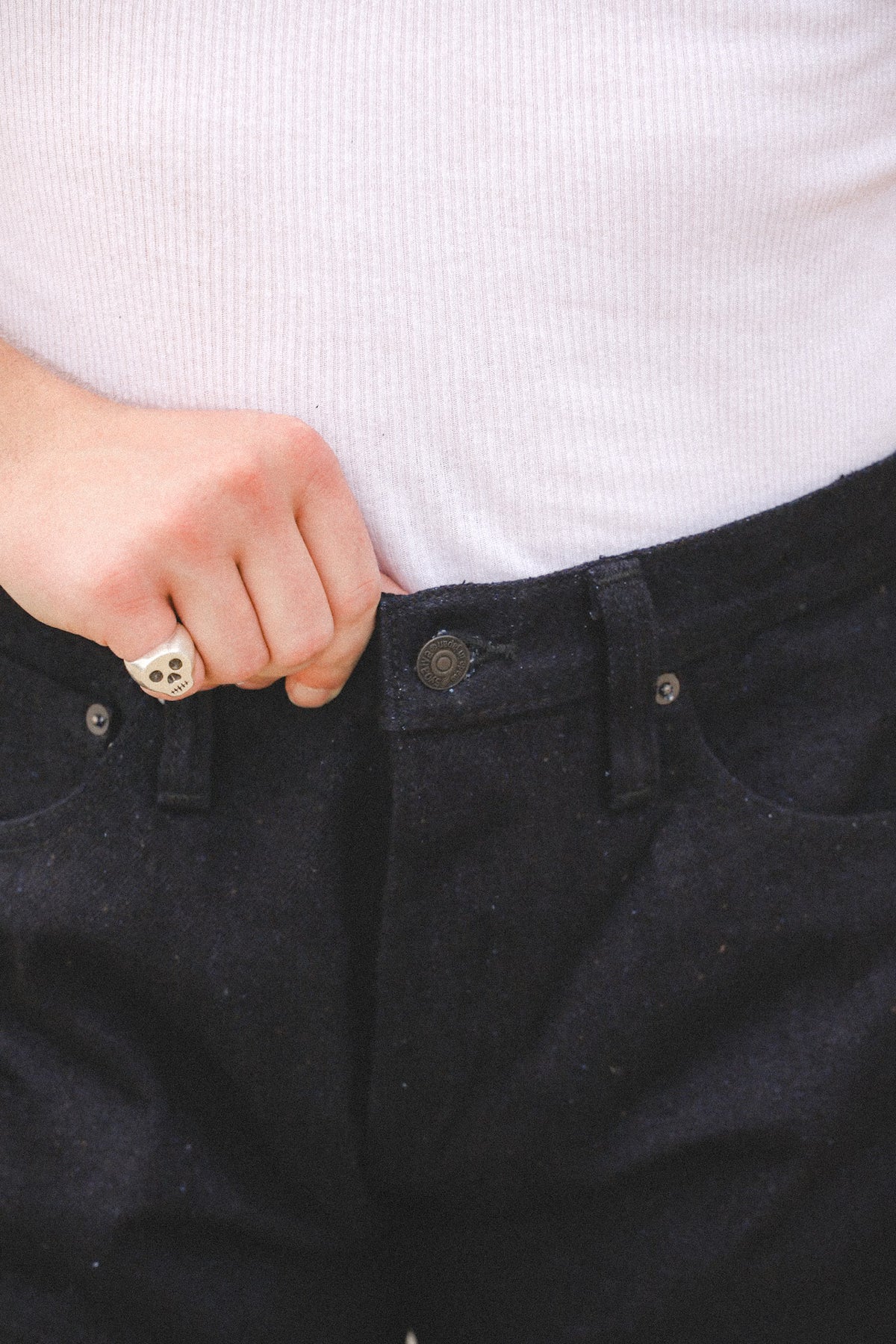 Close-up of a person wearing dark charcoal gray or black denim jeans with a white ribbed knit top, showing the button closure and waistband.
