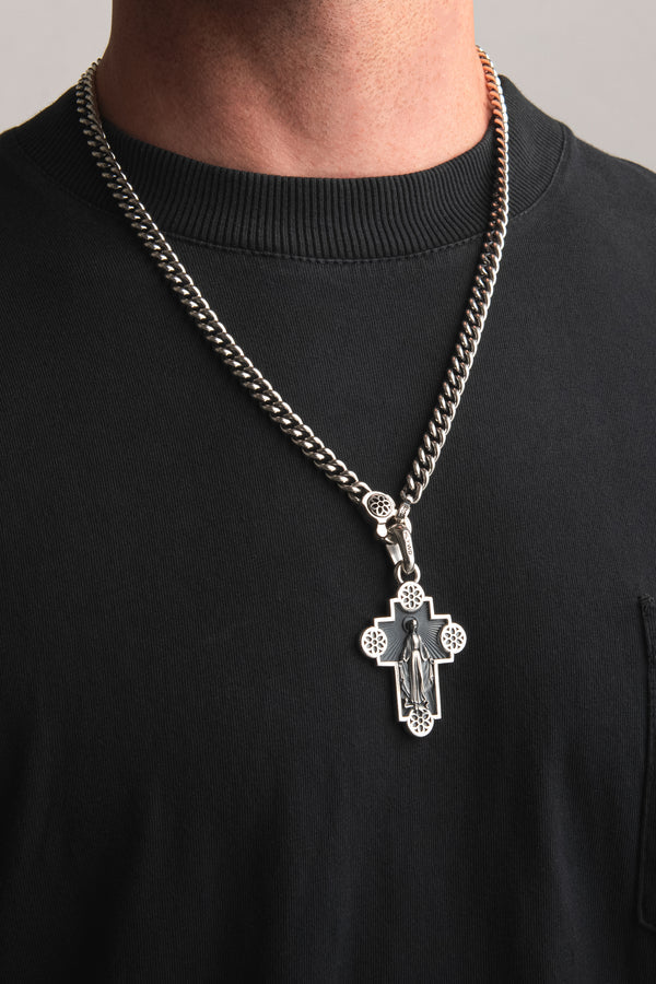 Close-up of a men's thick silver chain necklace with a detailed religious cross pendant worn over a black shirt