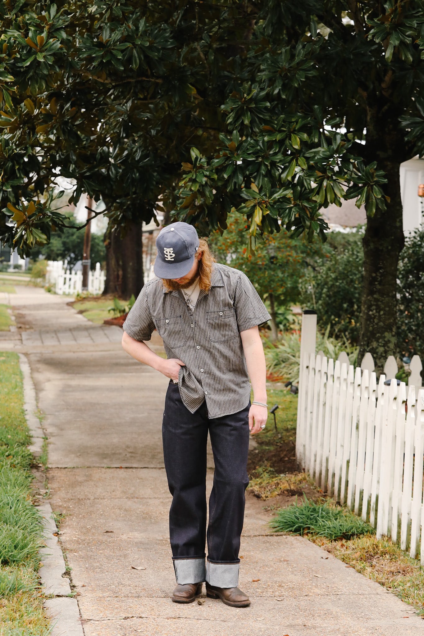 Person walking on a sidewalk with trees and a white picket fence in the background