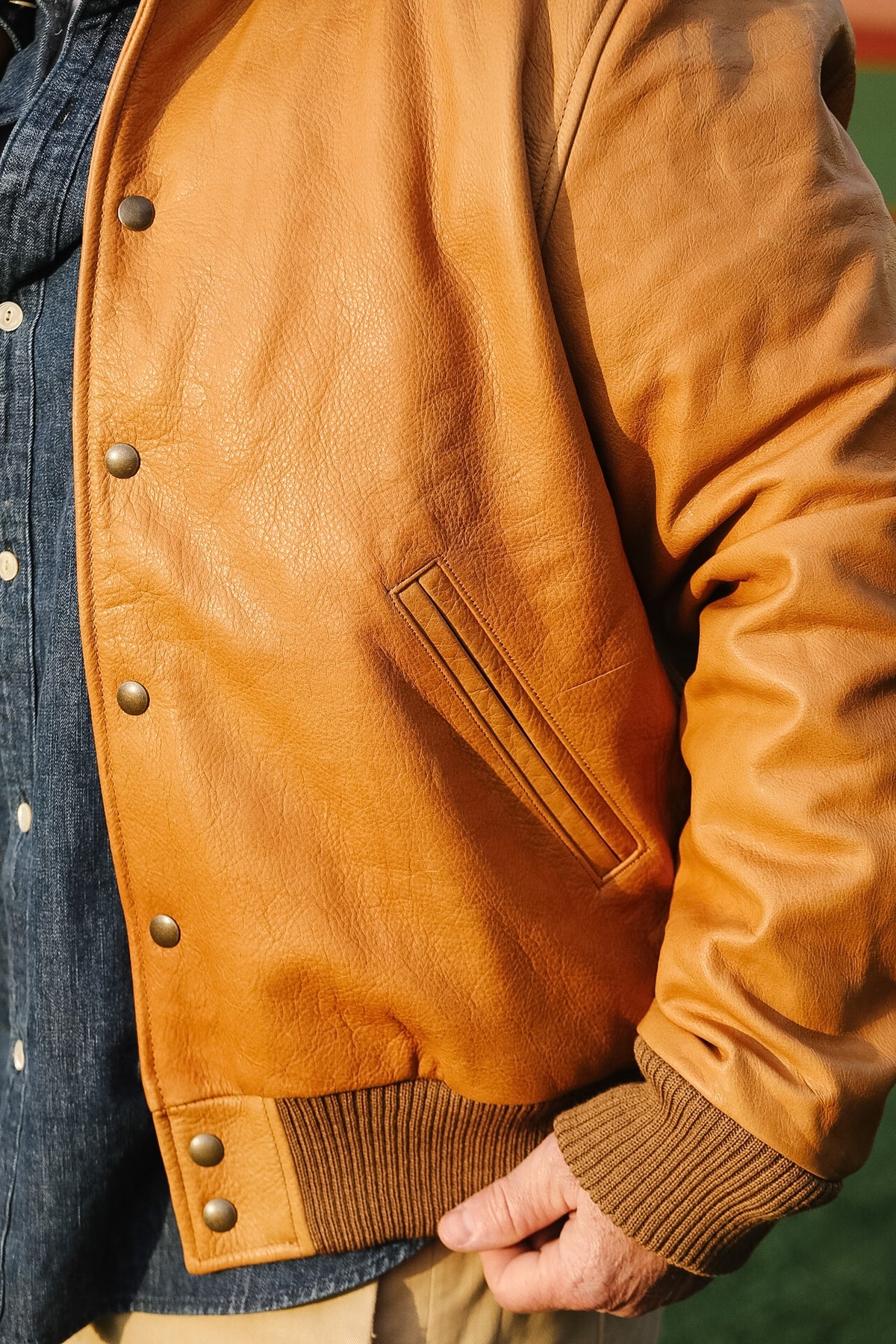 Close-up of a brown leather jacket with a person wearing it.