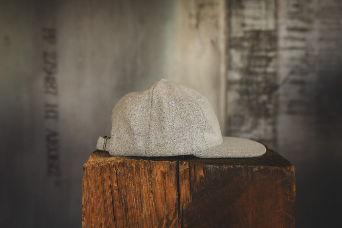 A light beige textured baseball cap with a matching flat visor, resting on a rustic wooden block against a dark, textured background.