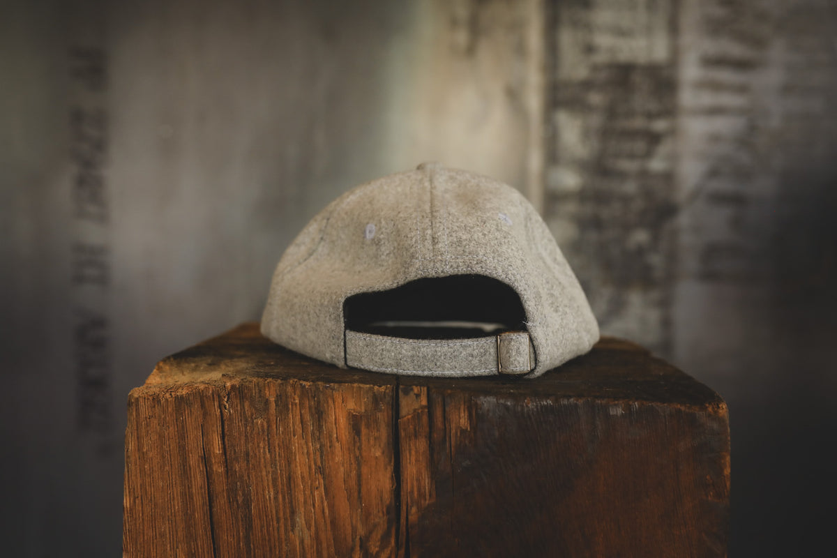 A light beige textured baseball cap with a dark interior and adjustable strap, displayed on a rustic wooden block against a blurred gray background.