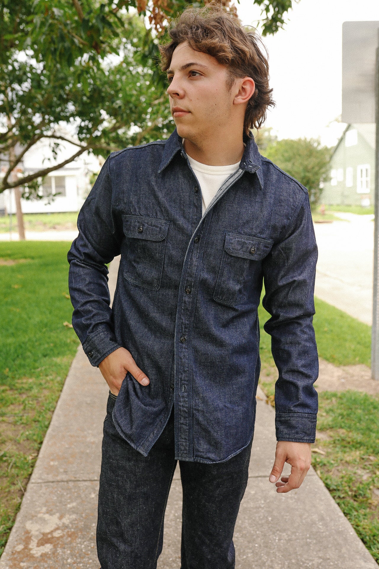 Man wearing indigo denim medical shirt with button pockets, standing outdoors on sidewalk
