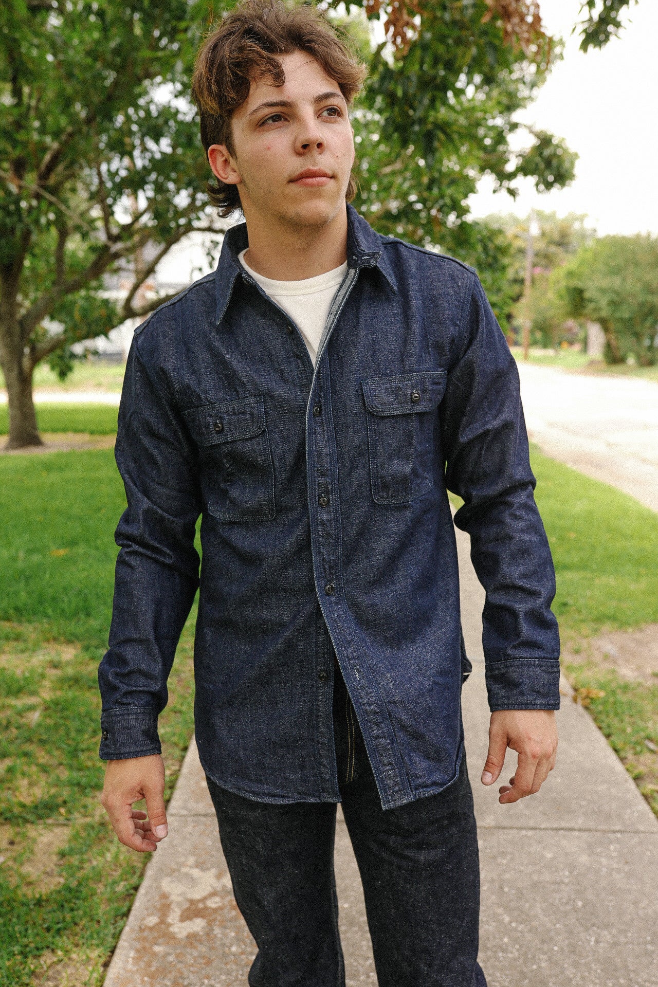Young man wearing Indigo denim medical shirt with button pockets walking outdoors on sidewalk