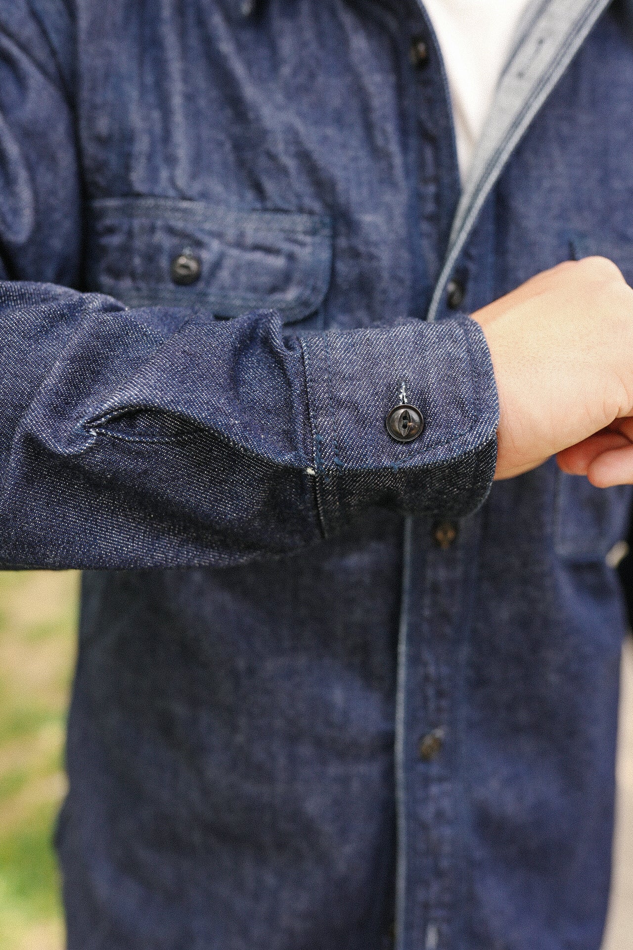 Close-up of person wearing indigo denim medical shirt with buttoned cuff and chest pocket flap