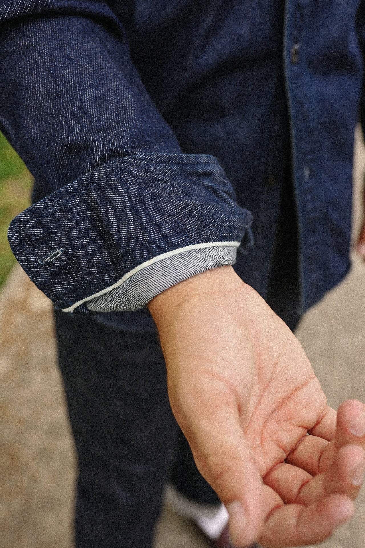 Close-up of a person wearing an indigo denim shirt with rolled-up sleeves showing selvedge edge detail