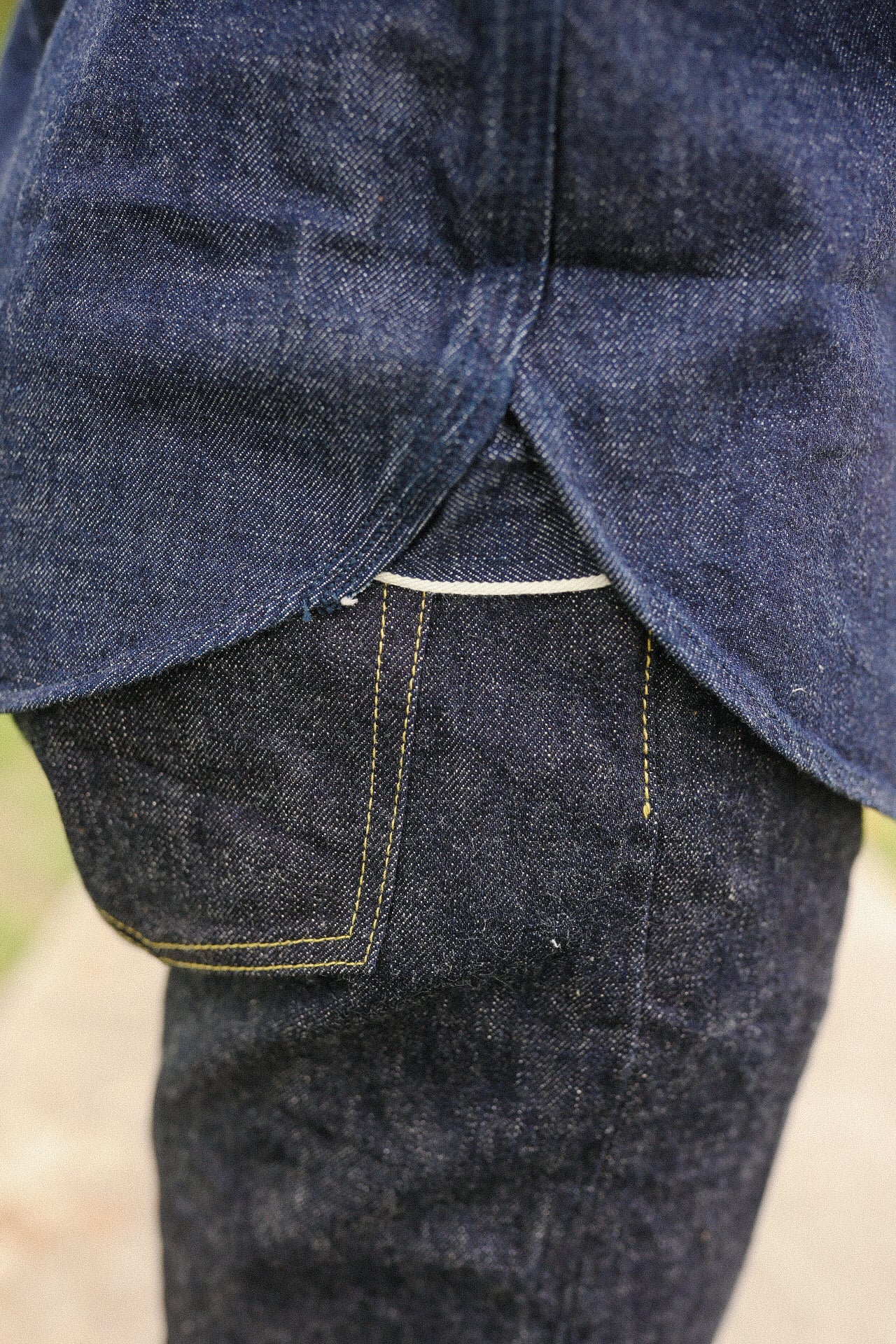 Close-up of indigo denim medical shirt overlapping raw selvedge denim jeans with yellow stitching