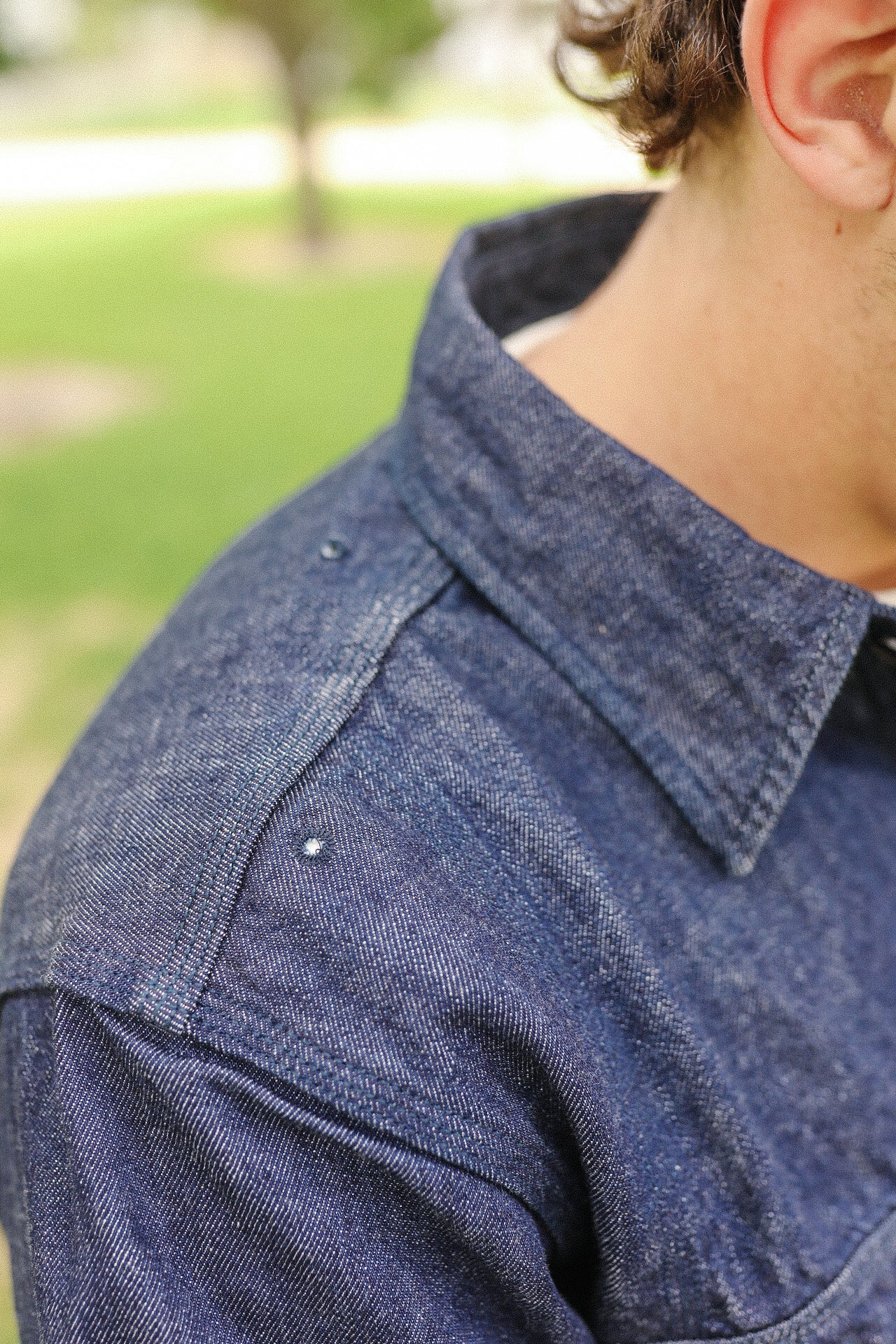 Close-up of indigo denim medical shirt shoulder and collar with metal rivets outdoors