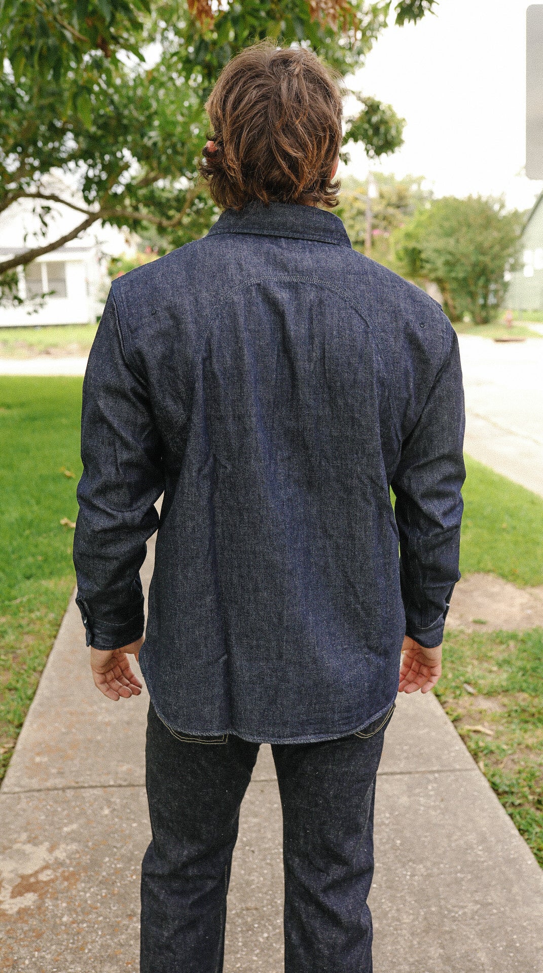 Man wearing indigo denim medical shirt and black denim jeans standing outdoors on sidewalk