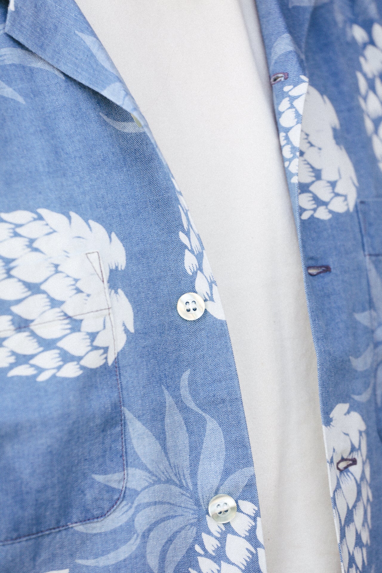 Close-up of Duke Kahanamoku indigo cotton Hawaiian shirt with white pineapple print and pearl buttons