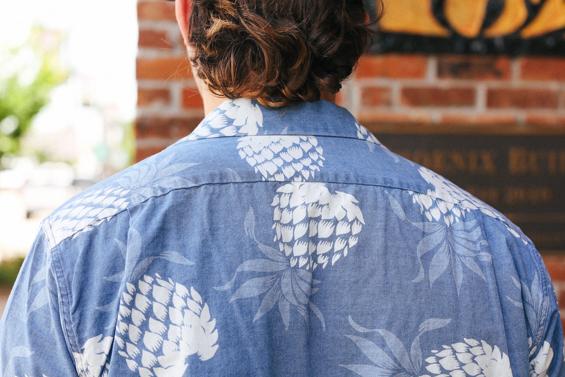 Back view of a person wearing a blue indigo cotton Hawaiian shirt with white pineapple print