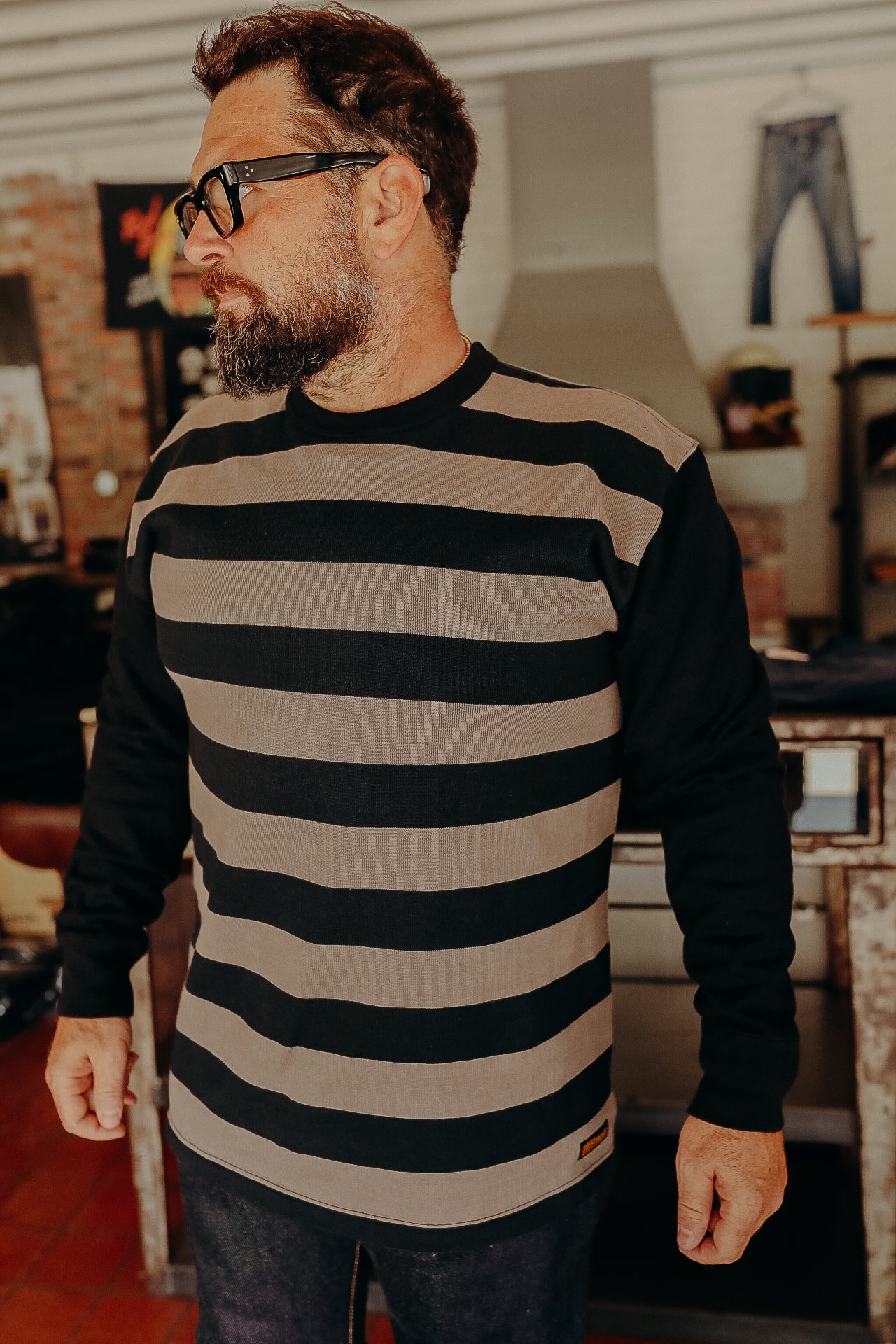 Bearded man wearing black and brown striped long sleeve shirt in rustic indoor setting at Iron Shop Provisions