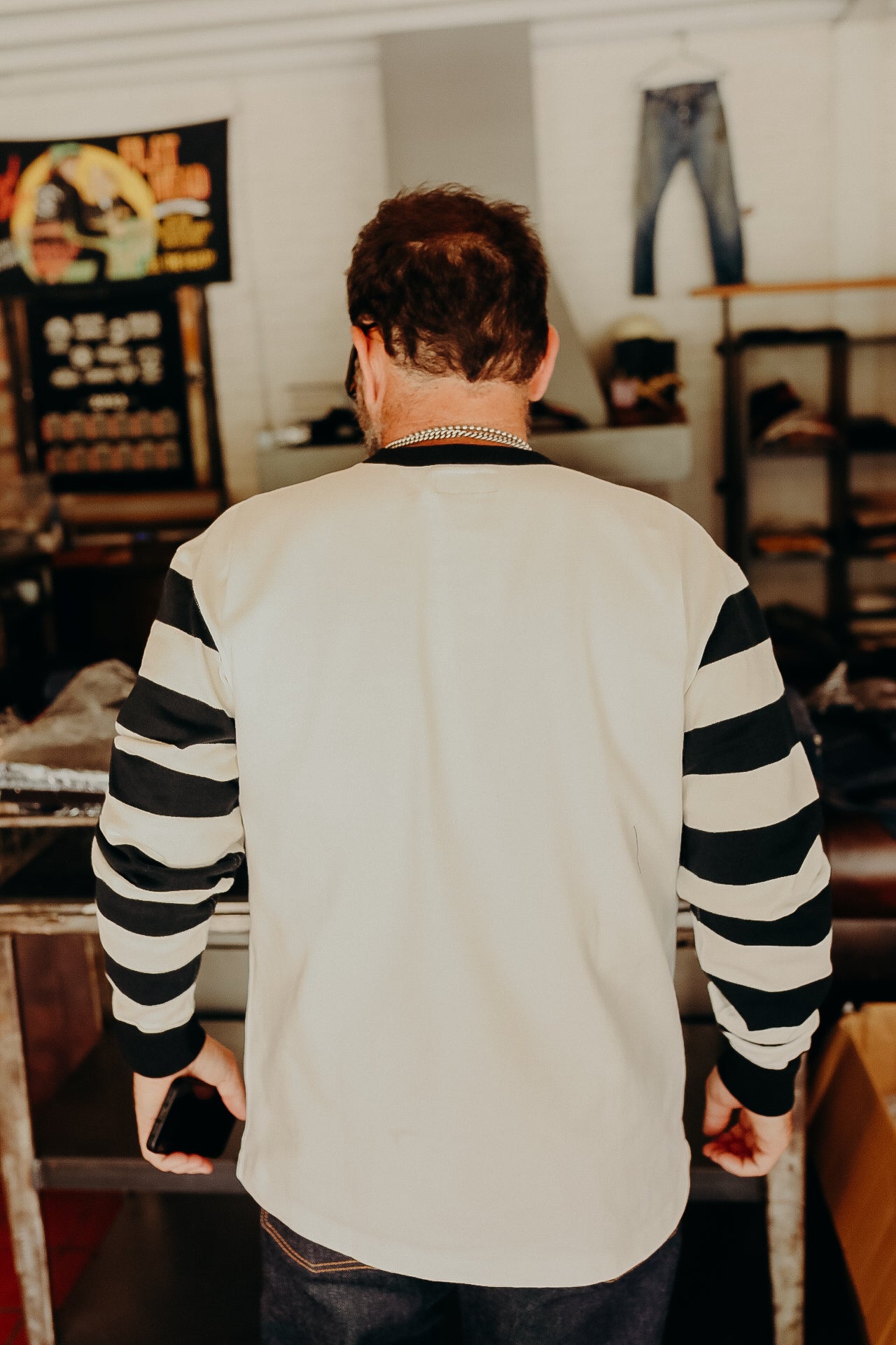 Man wearing a long-sleeve white shirt with black horizontal stripes on sleeves inside a denim store