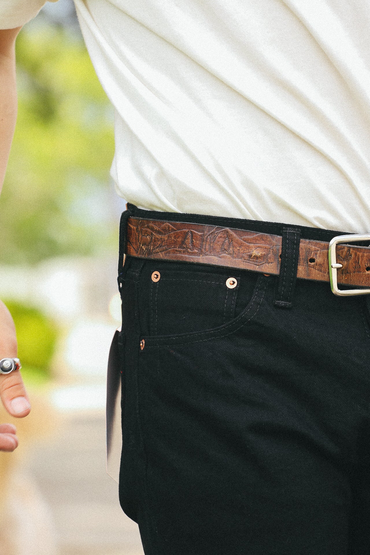 Close-up of person wearing black pants and a brown leather belt with mountain design, white shirt
