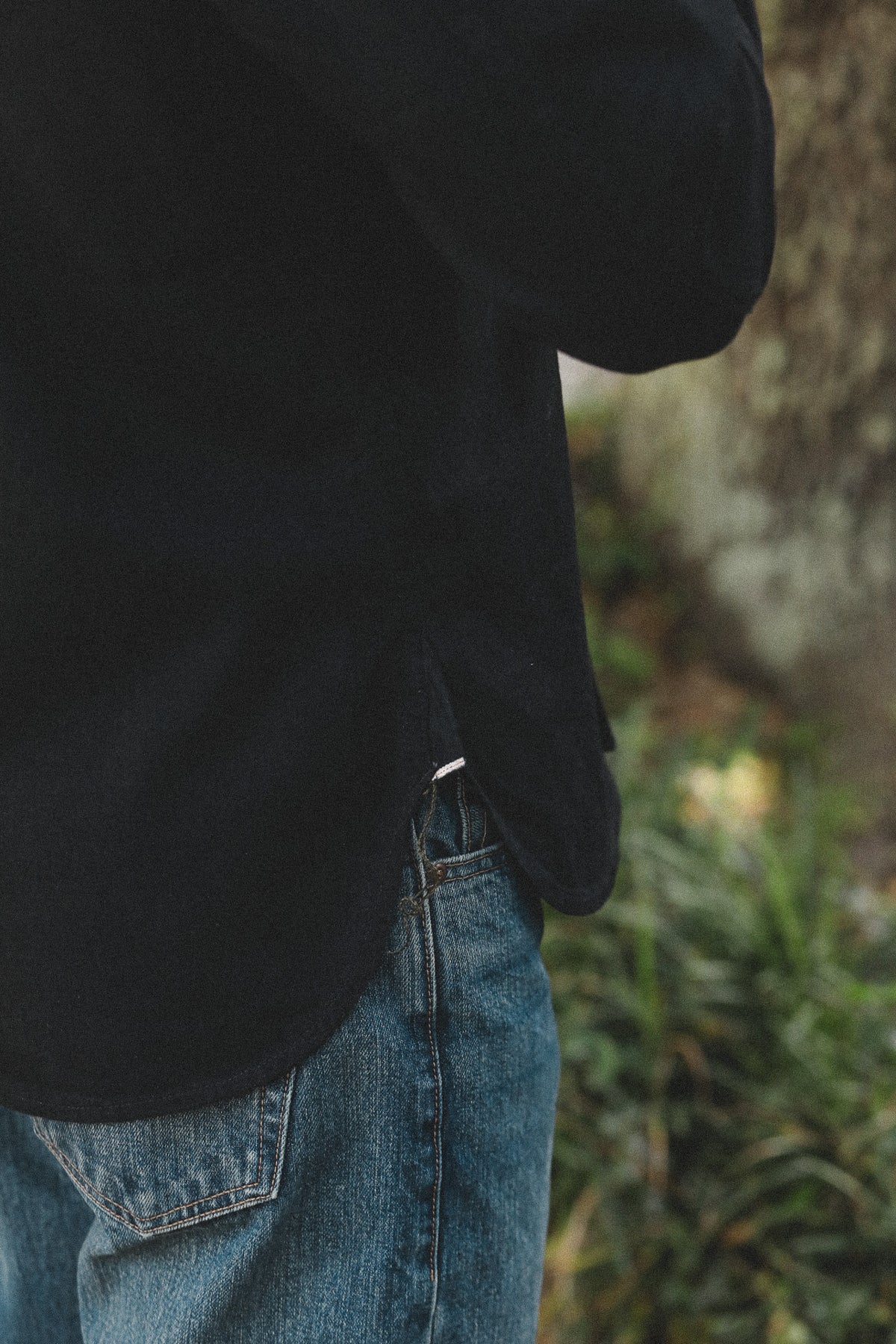 Person wearing a black jacket and blue jeans standing in a natural setting.