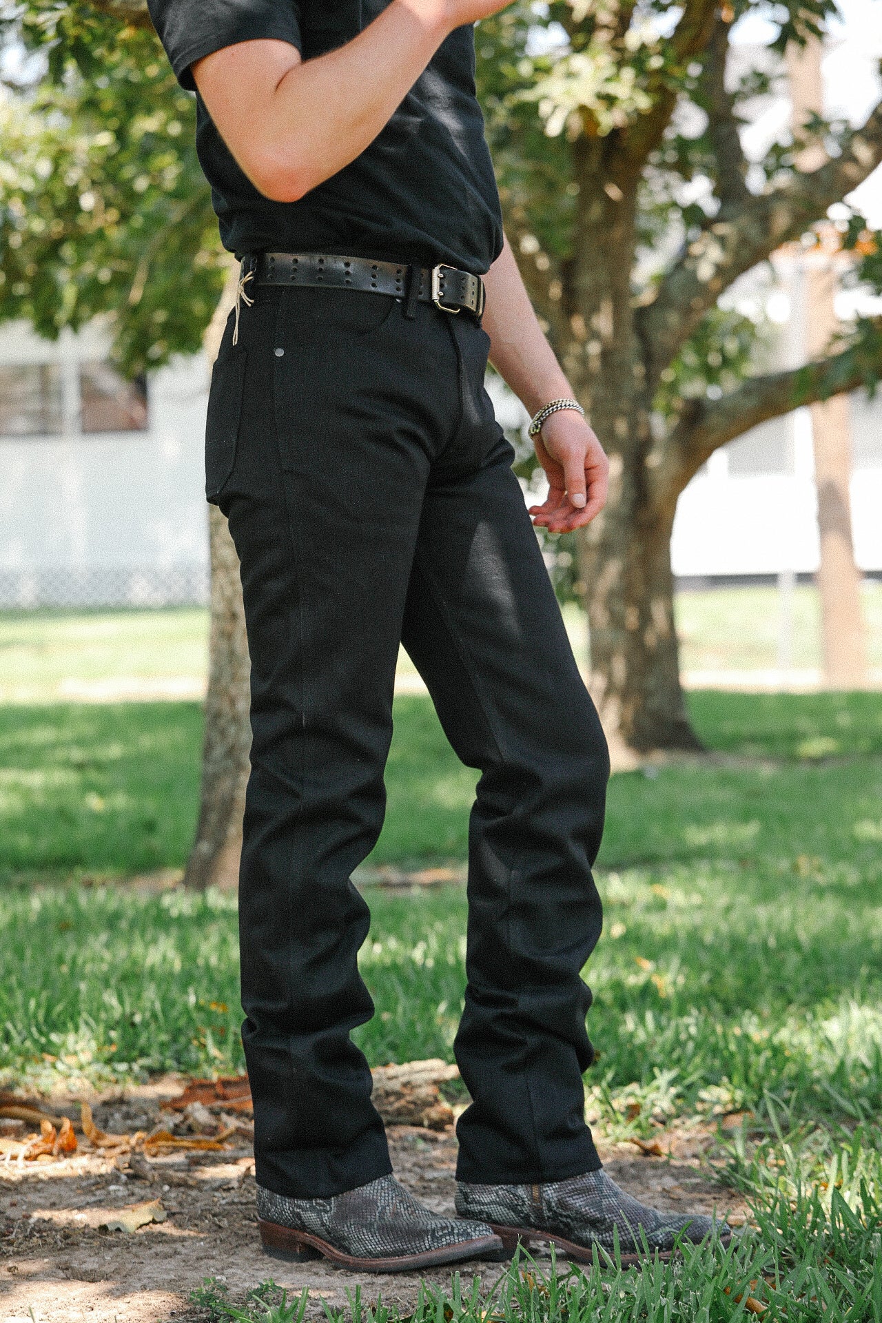 Person wearing black jeans, black perforated leather belt, and gray snakeskin boots outdoors on grass