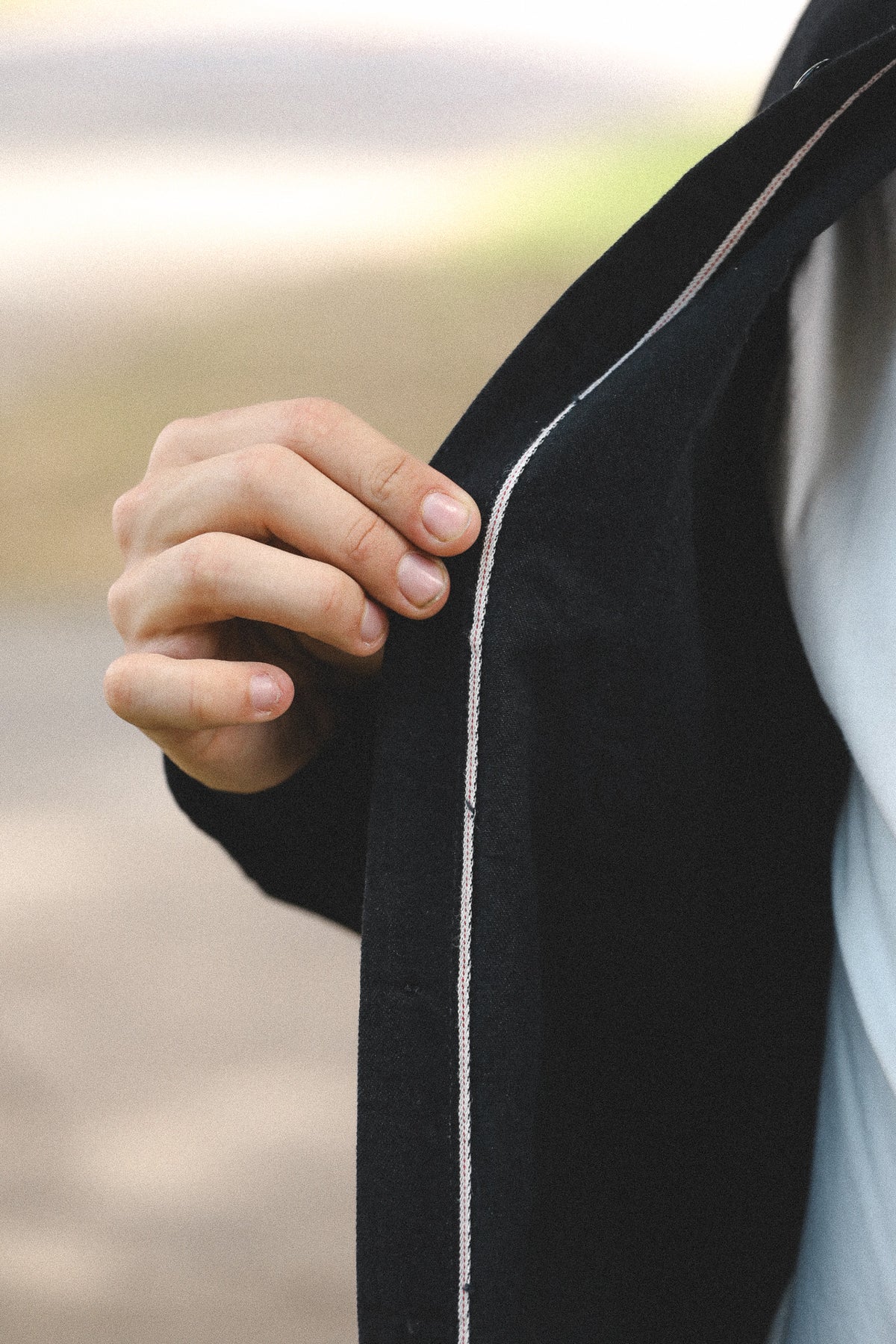 Close-up of a hand holding a black garment with white piping.
