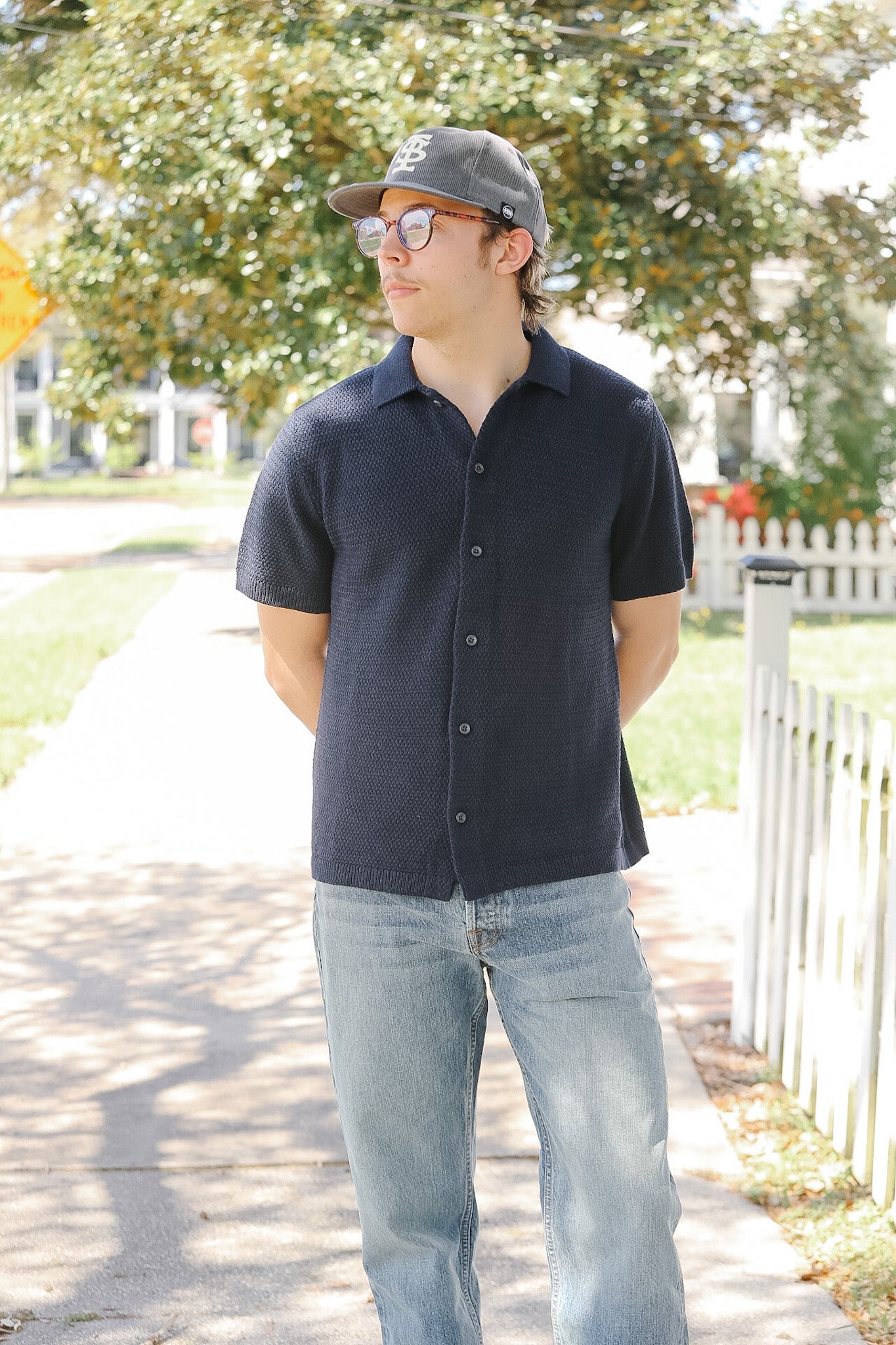 Man wearing a black shirt and cap outdoors with trees and a fence in the background