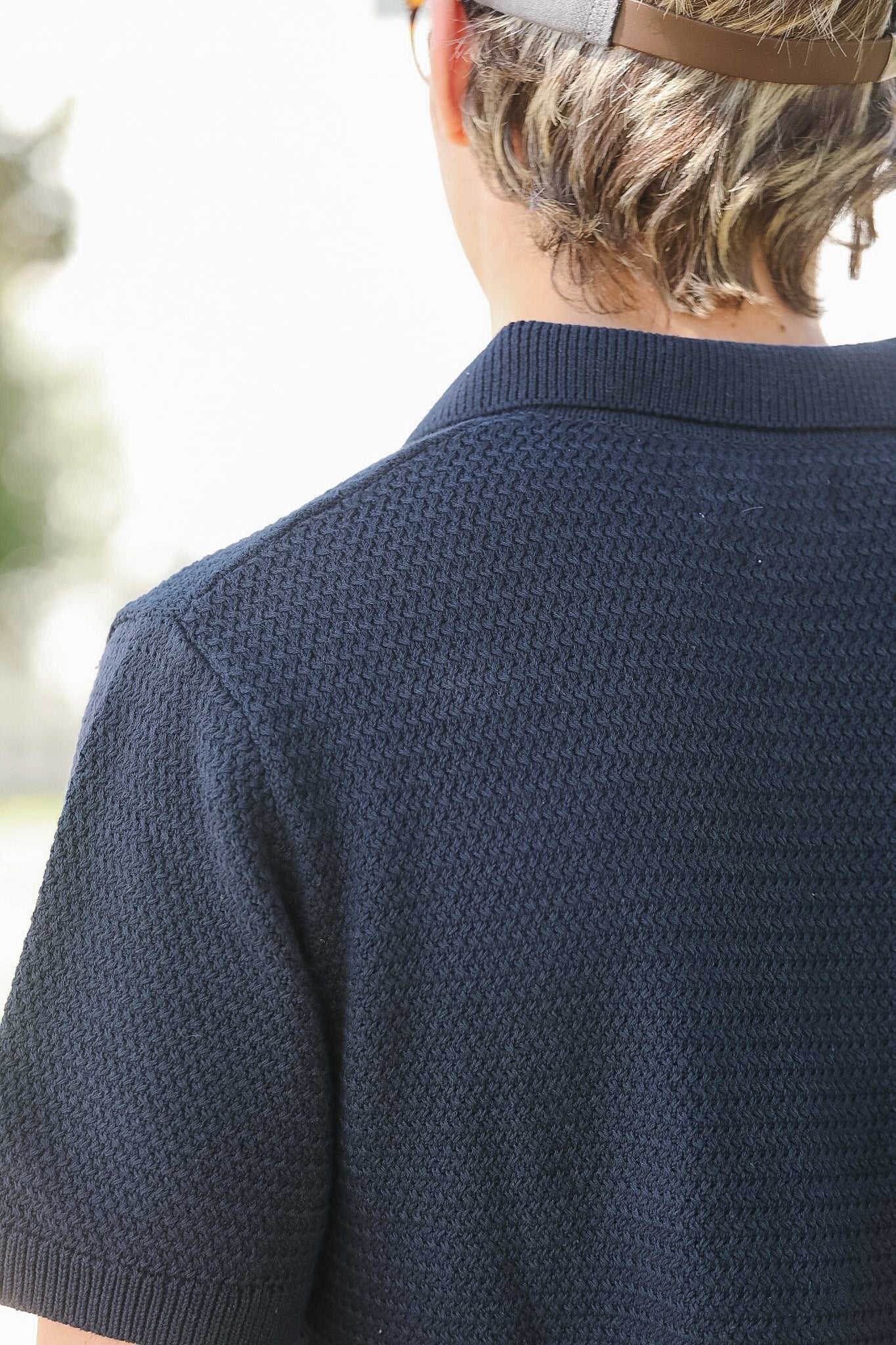 Person wearing a navy blue textured polo shirt with blurred background