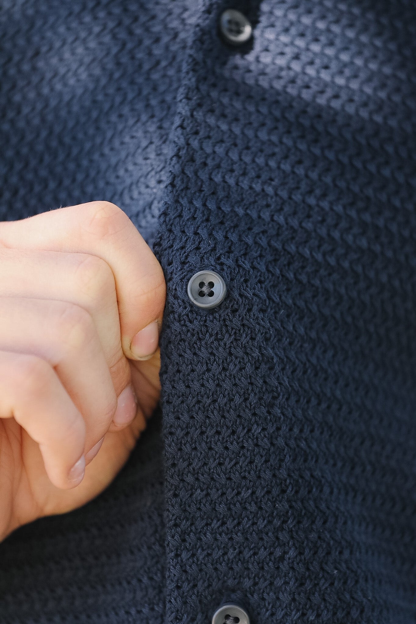 Close-up of a hand pressing a button on a dark blue textured fabric.