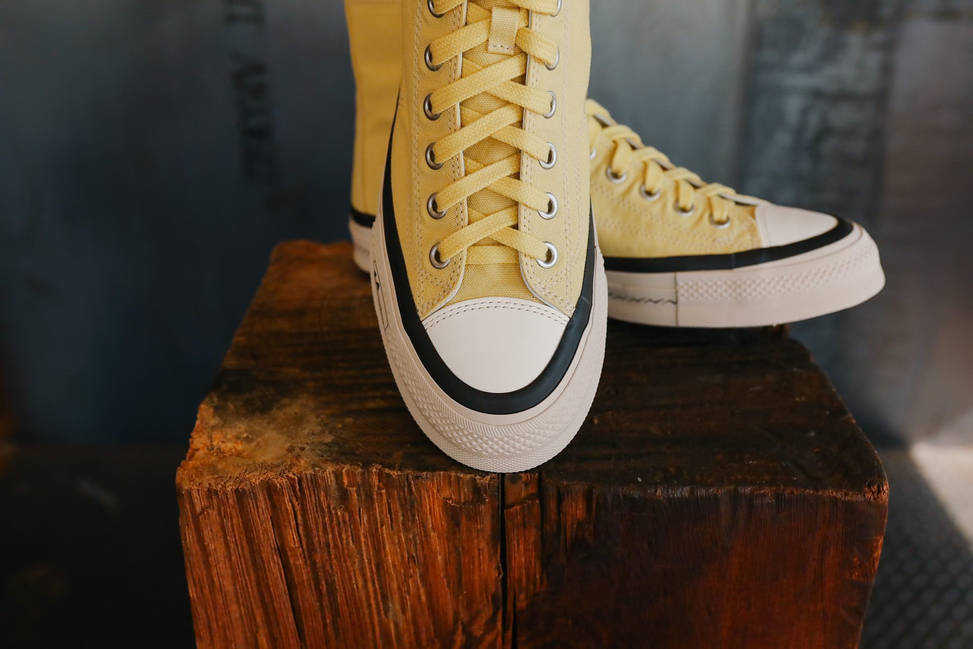Yellow high-top sneakers with white soles on a wooden block against a blurred background