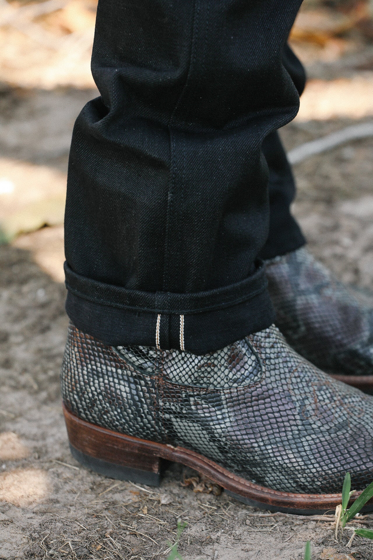 Close-up of reptile-patterned leather boots with wooden heels worn with black denim jeans outdoors