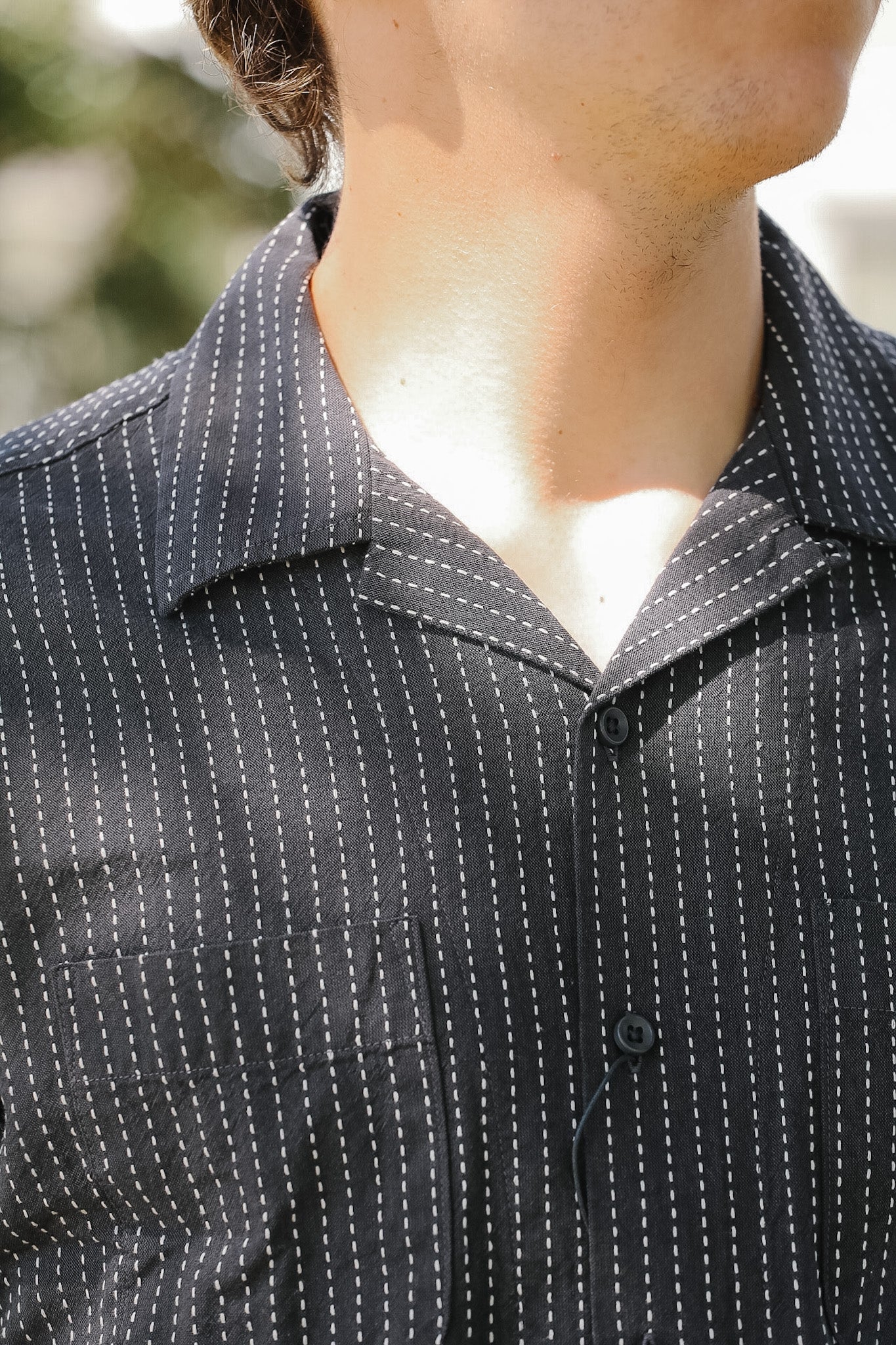 Close-up of a person wearing a black pinstripe shirt with a blurred background
