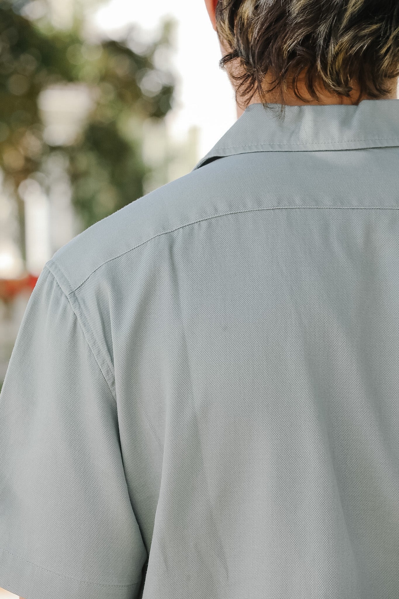 Person wearing a light gray shirt with a blurred outdoor background