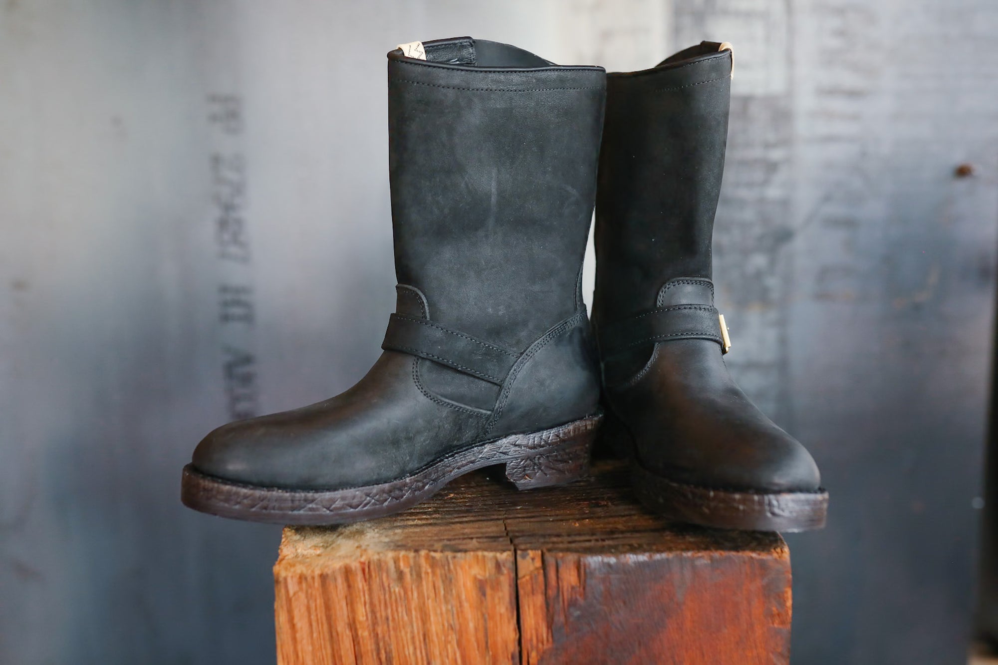 Pair of black leather boots on a wooden block against a textured gray background