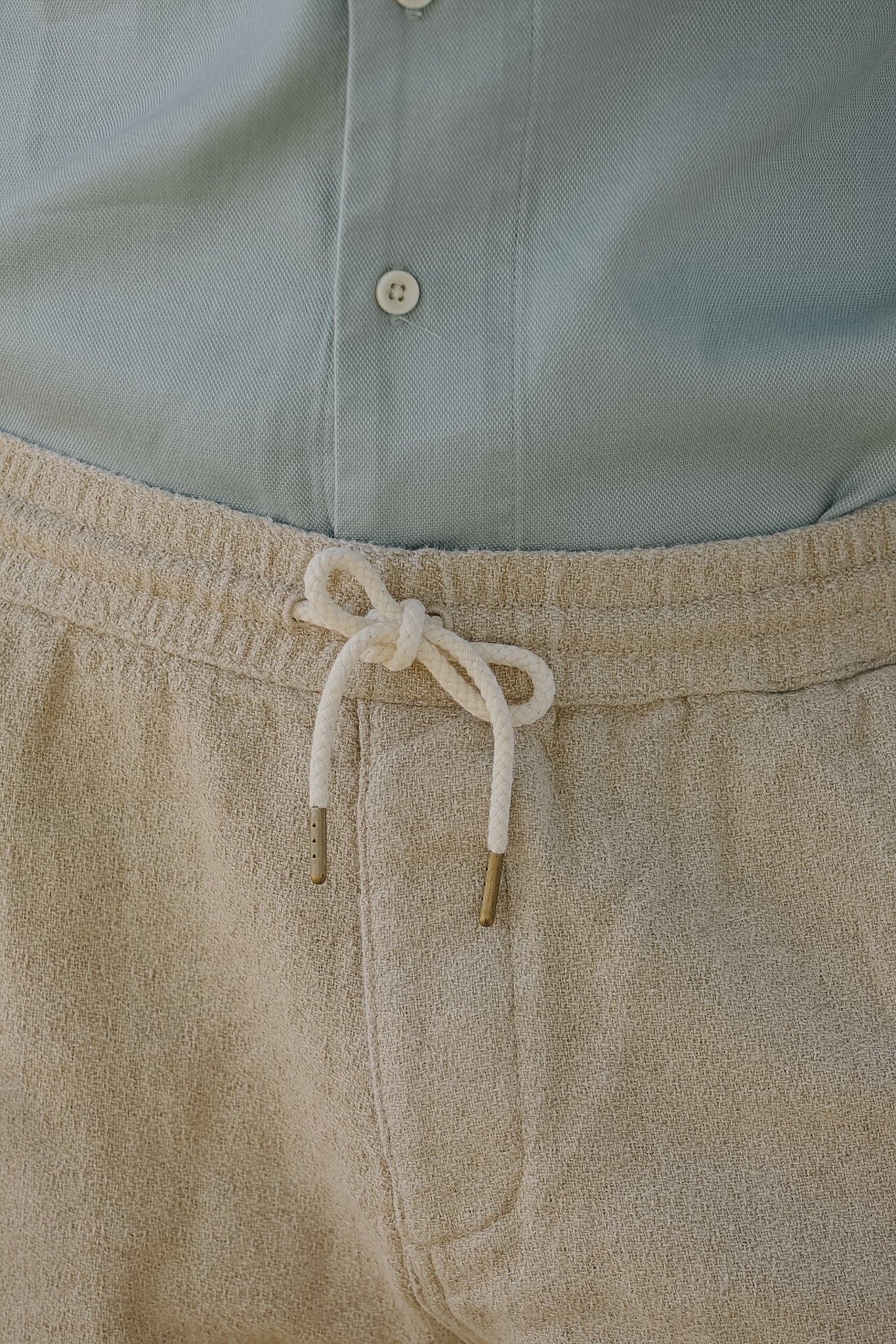 Close-up of beige pants with a drawstring and light blue shirt.